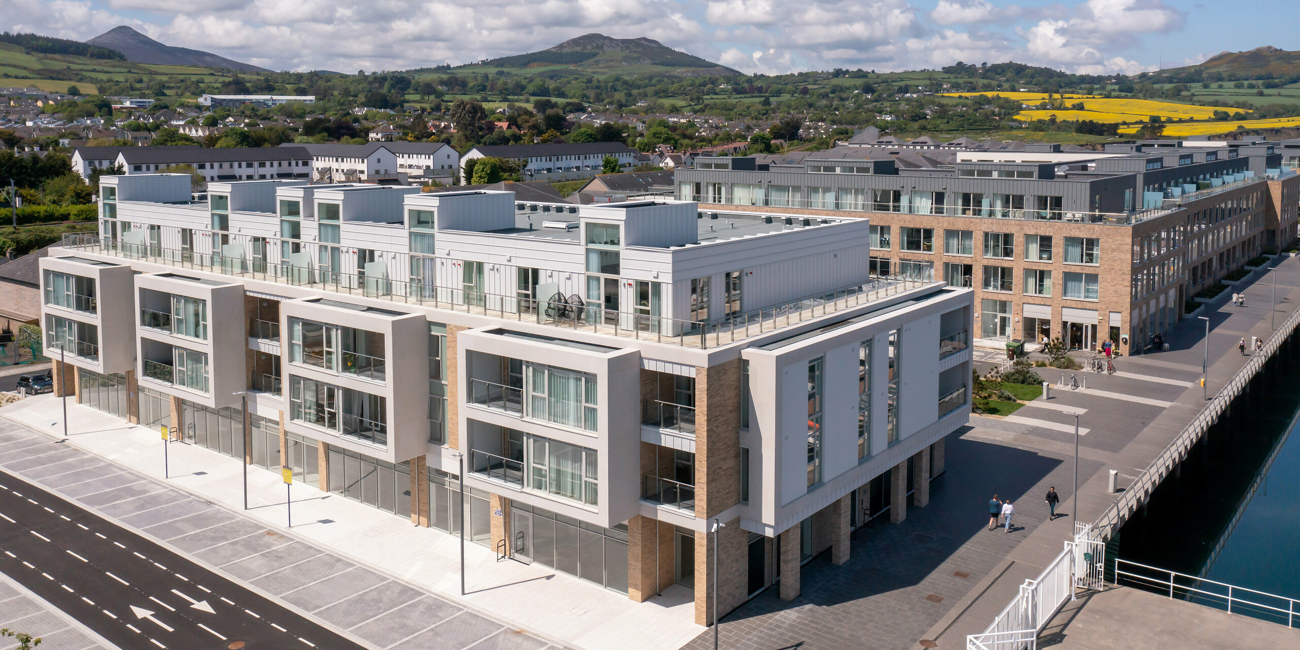 Marina Village Greystones à Wicklow, Irlande - Prise de vue grand angle d'un lotissement moderne en bord de mer surplombant la marina. Le complexe immobilier est revêtu d'environ 2 000 m² de PREFALZ robuste dans les couleurs P.10 Prefa blanc et P.10 gris souris. L'architecture élégante comprend de grandes façades vitrées, des balcons spacieux et une façade esthétique. Entouré d'un paysage pittoresque et de tôles de haute qualité PREFA, le village offre une protection durable et une esthétique intemporelle pour une vie exclusive au bord de la mer.