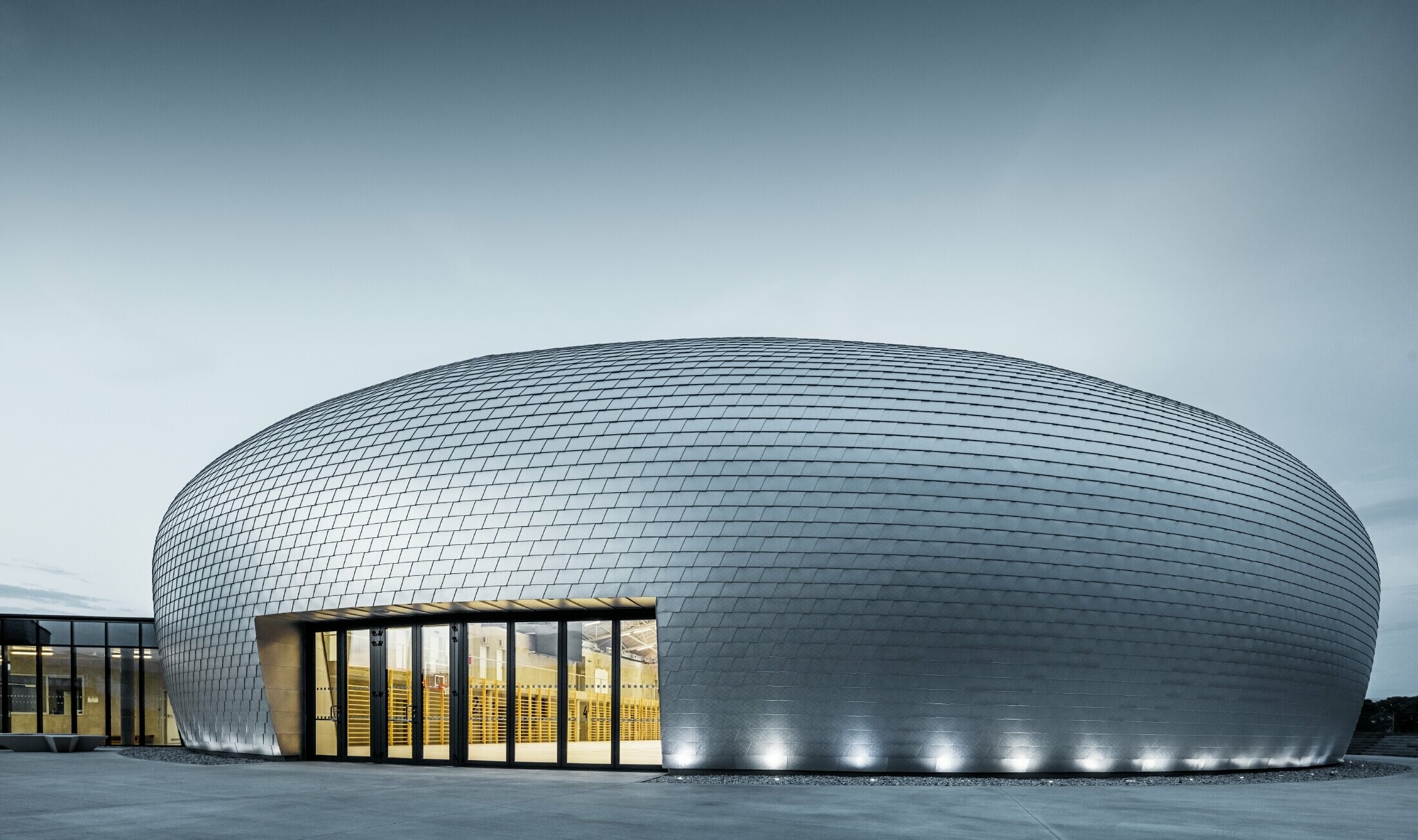 Vue du gymnase en République tchèque semblable à un OVNI recouvert de bardeaux de façade PREFA en alu brillant naturel.