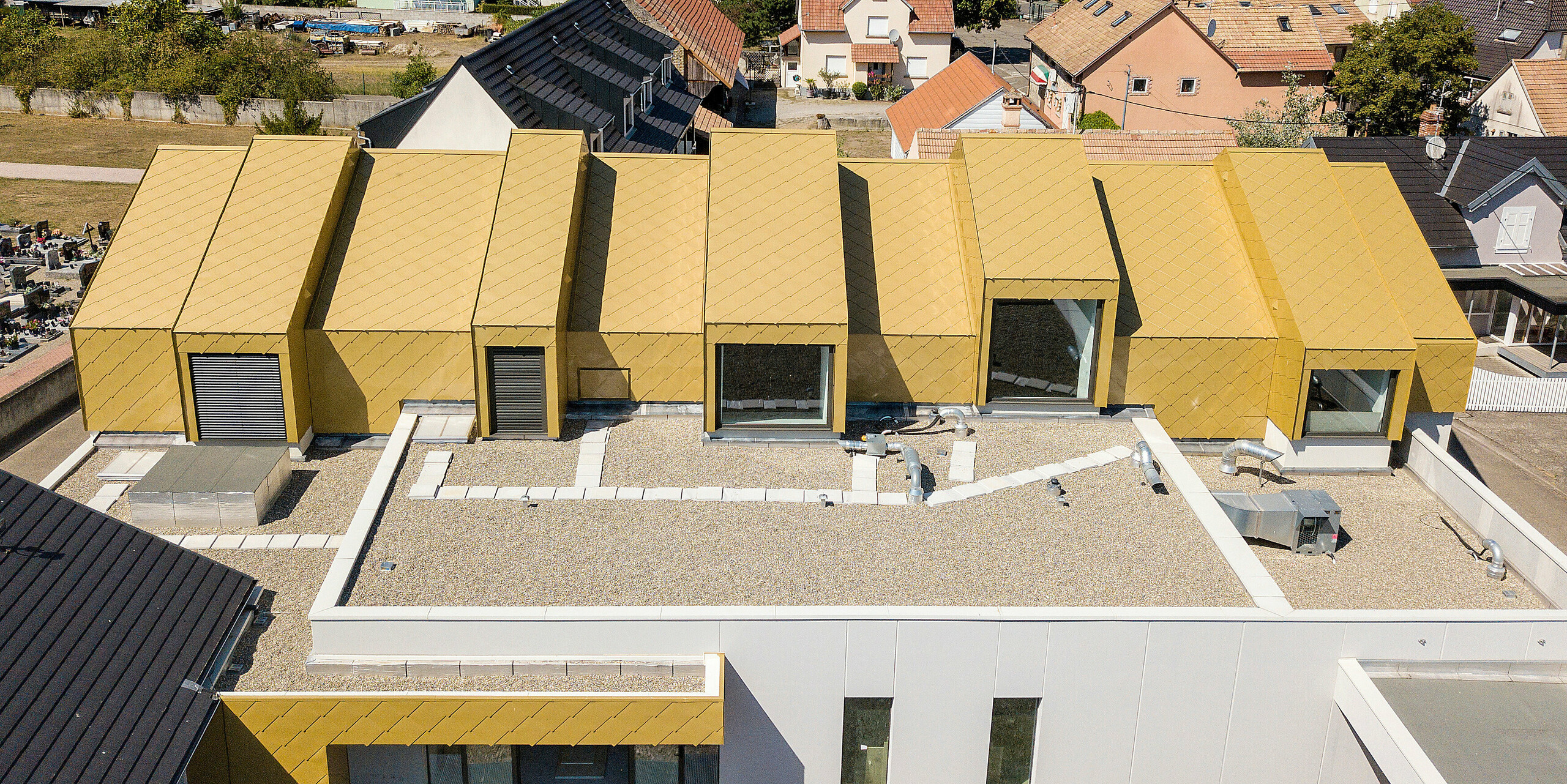 Vue plongeante sur le toit du centre communautaire et culturel de Fessenheim, France. Le toit et certaines parties de la façade ont été revêtus de losanges de toiture et façade PREFA 44 × 44 en Sparkling Gold.