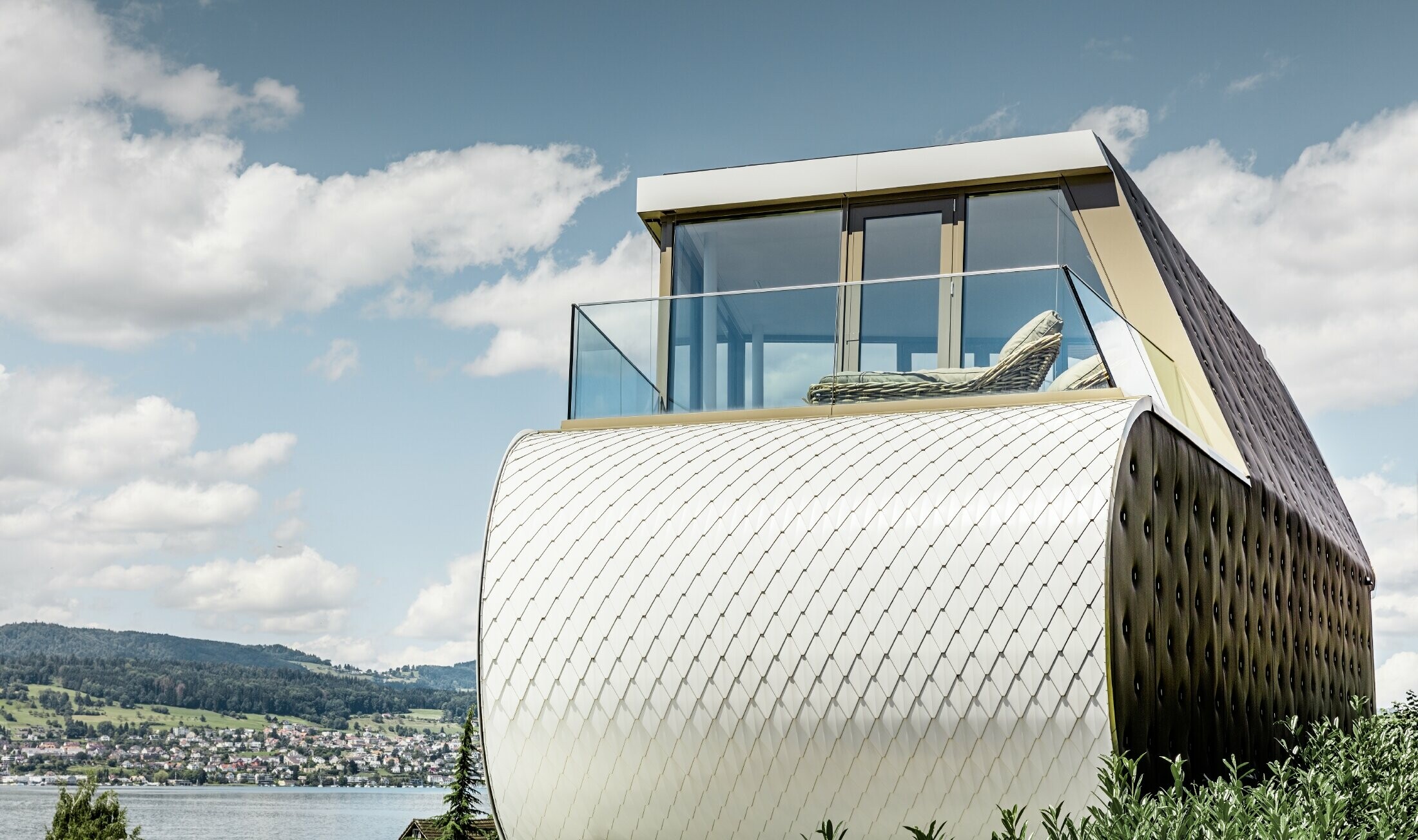 Vue latérale de la remarquable Flexhouse, conçue par l’architecte Camenzind. On voit l’un des murs extérieurs incurvés, revêtu de la façade en aluminium en écailles de PREFA, couleur blanc pur.