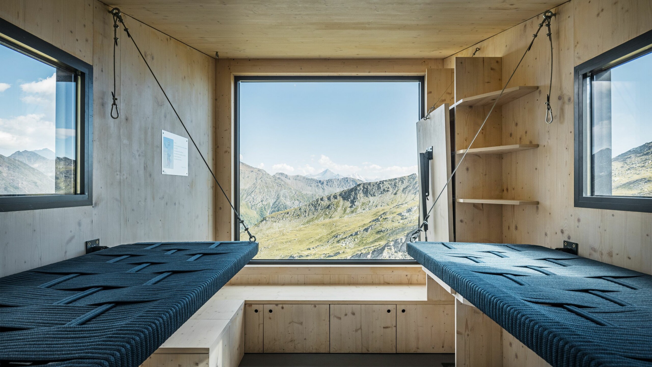 Prise de vue de l'intérieur comprenant un espace de couchage et de rangement, les fenêtres offrent une vue lointaine sur un paysage naturel à couper le souffle.