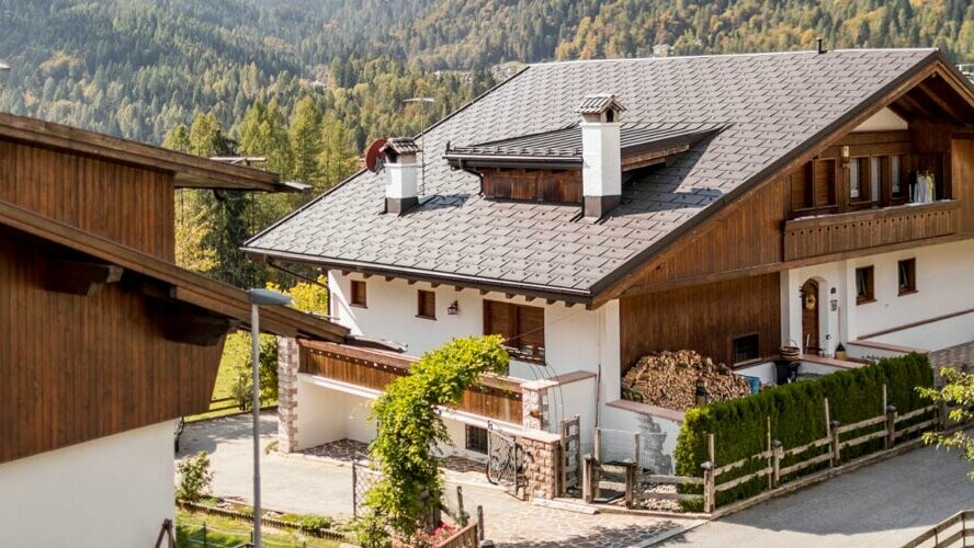 Maison traditionnelle avec couverture de toit PREFA brun noisette et façade avec éléments en bois et crépi