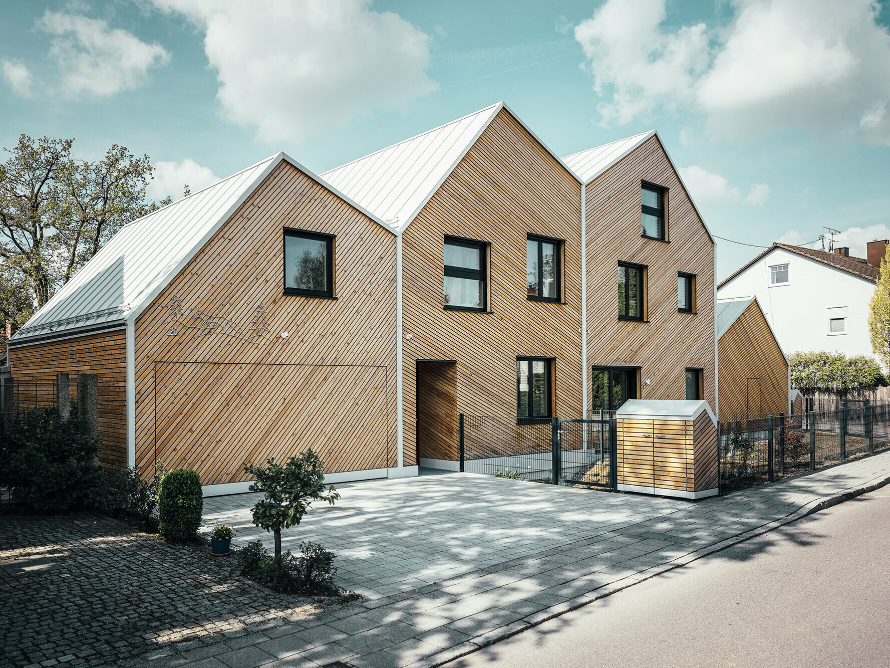 Seitliche Straßenansicht Hausfuchs mit Blick auf die unregelmäßige Dachlandschaft, Fassade mit Lärchenholzschalung, Müllhäuschen