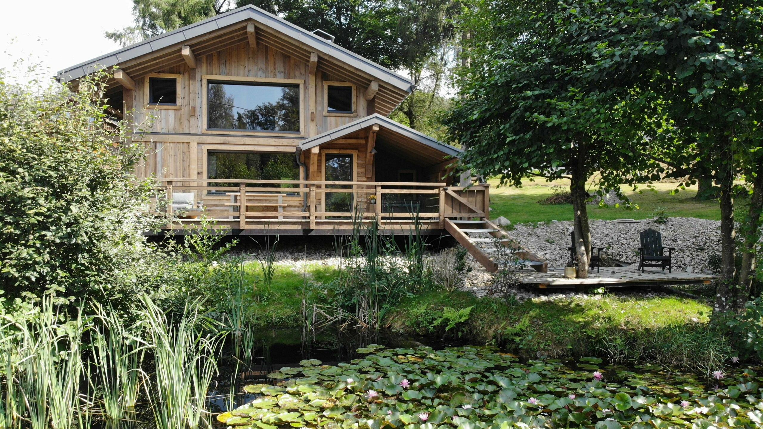 Prise de vue depuis l'étang, des nénuphars recouvrent sa surface. En fond, le gîte La Cabane à Sucre dont la couverture a été faite en R.16 PREFA