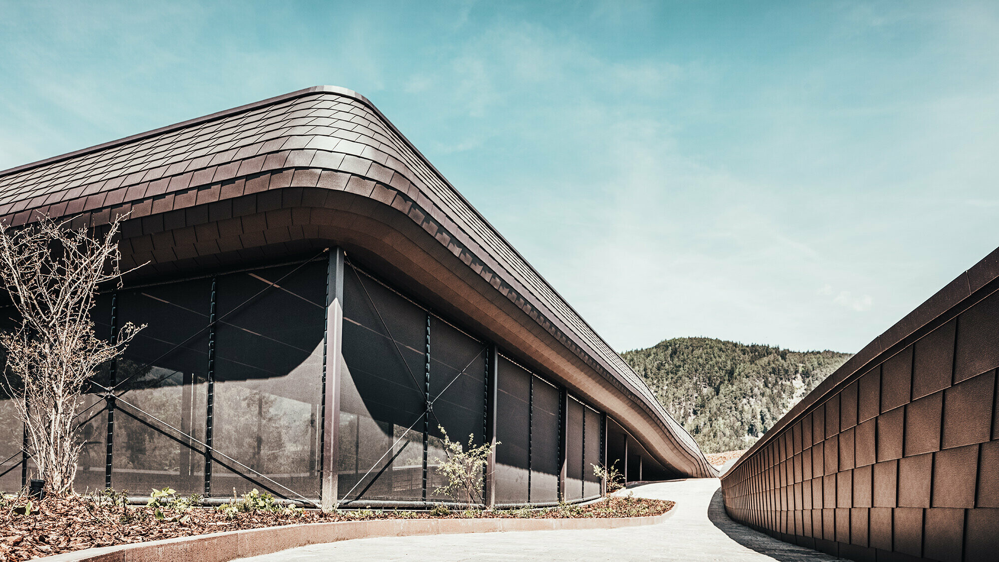 Prise de vue du côté de l'extérieur de l'hôtel du Tyrol du sud. Les bardeaux de façade prefa se voient sur toutes les surfaces. En arrière-plan, le paysages est vallonné et arboré.