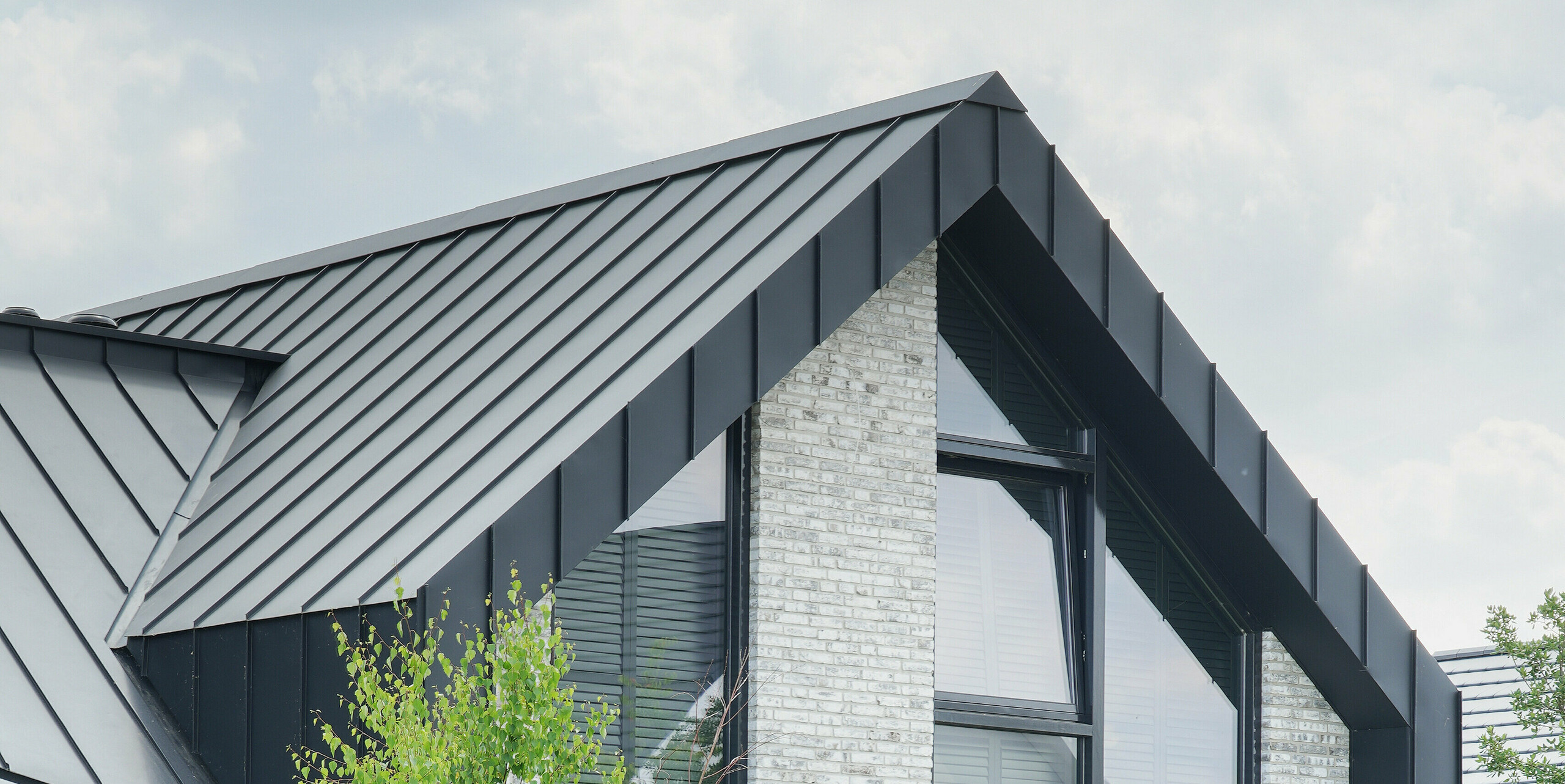 Vue partielle d'un immeuble d'habitation moderne à Veenendaal, aux Pays-Bas, avec la façade noire du bâtiment PREFALZ. La combinaison de lignes de toit fortement inclinées et d'une façade structurée en pierre naturelle gris clair crée un jeu architectural captivant. De grandes fenêtres à hauteur de plafond égayent la façade et offrent une vue sur l'extérieur.