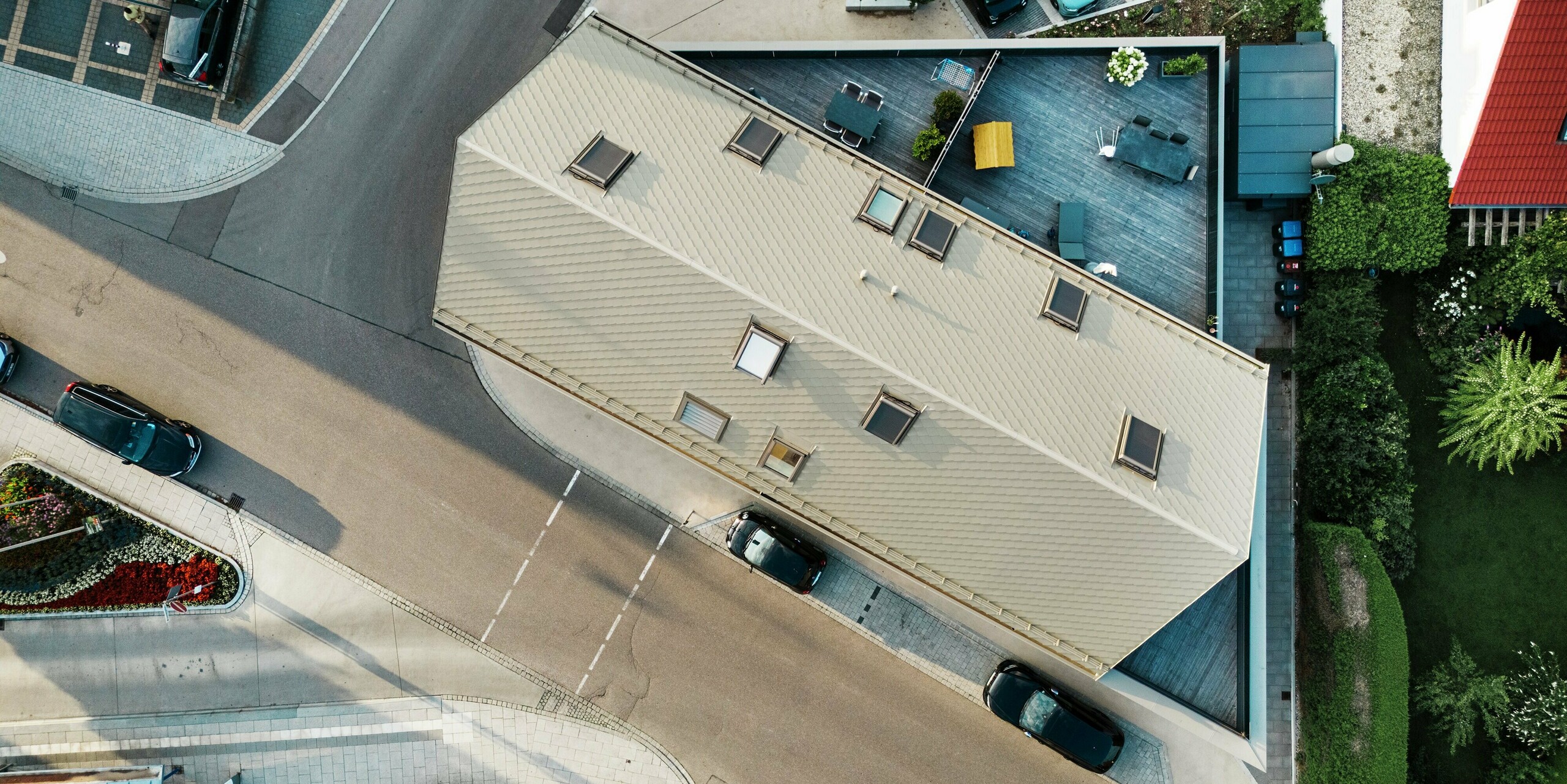 Vue plongeante sur un immeuble d'appartements à Leitershofen, en Allemagne, avec des losanges de toiture 29x29 PREFA en bronze. Le bâtiment moderne impressionne par son architecture innovante aux usages multiples et ses terrasses spacieuses sur le toit. Les losanges en aluminium durables offrent une surface résistante aux intempéries et s'intègrent harmonieusement dans l'environnement urbain.