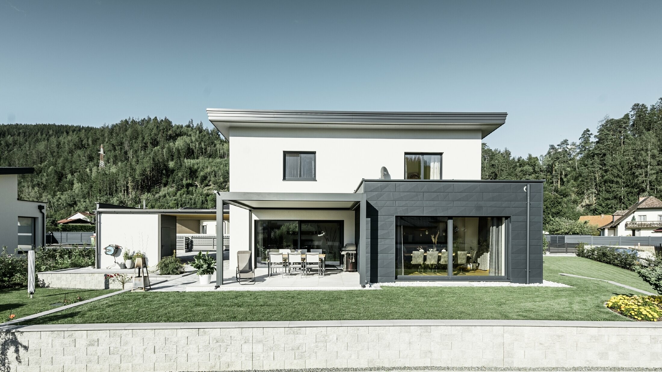 Neu gebautes Einfamilienhaus mit Zubau; Anbau hebt sich optisch vom Rest des Hauses ab, da er mit dem PREFA Fassadenpaneelen Siding.X in Anthrazit verkleidet ist. Der Rest der Fassade ist weiß verputzt.