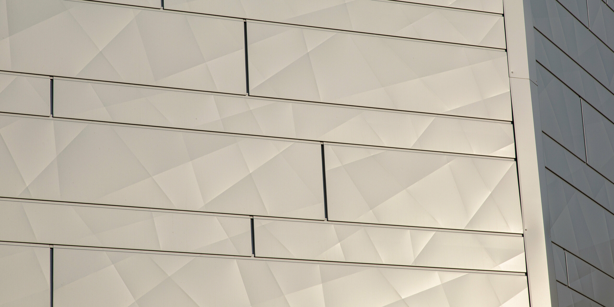 Vue détaillée du bord du bâtiment avec les panneaux de façade scintillants PREFA Siding.X en argent métallisé dans l'atelier AFFLELOU à Auray, France