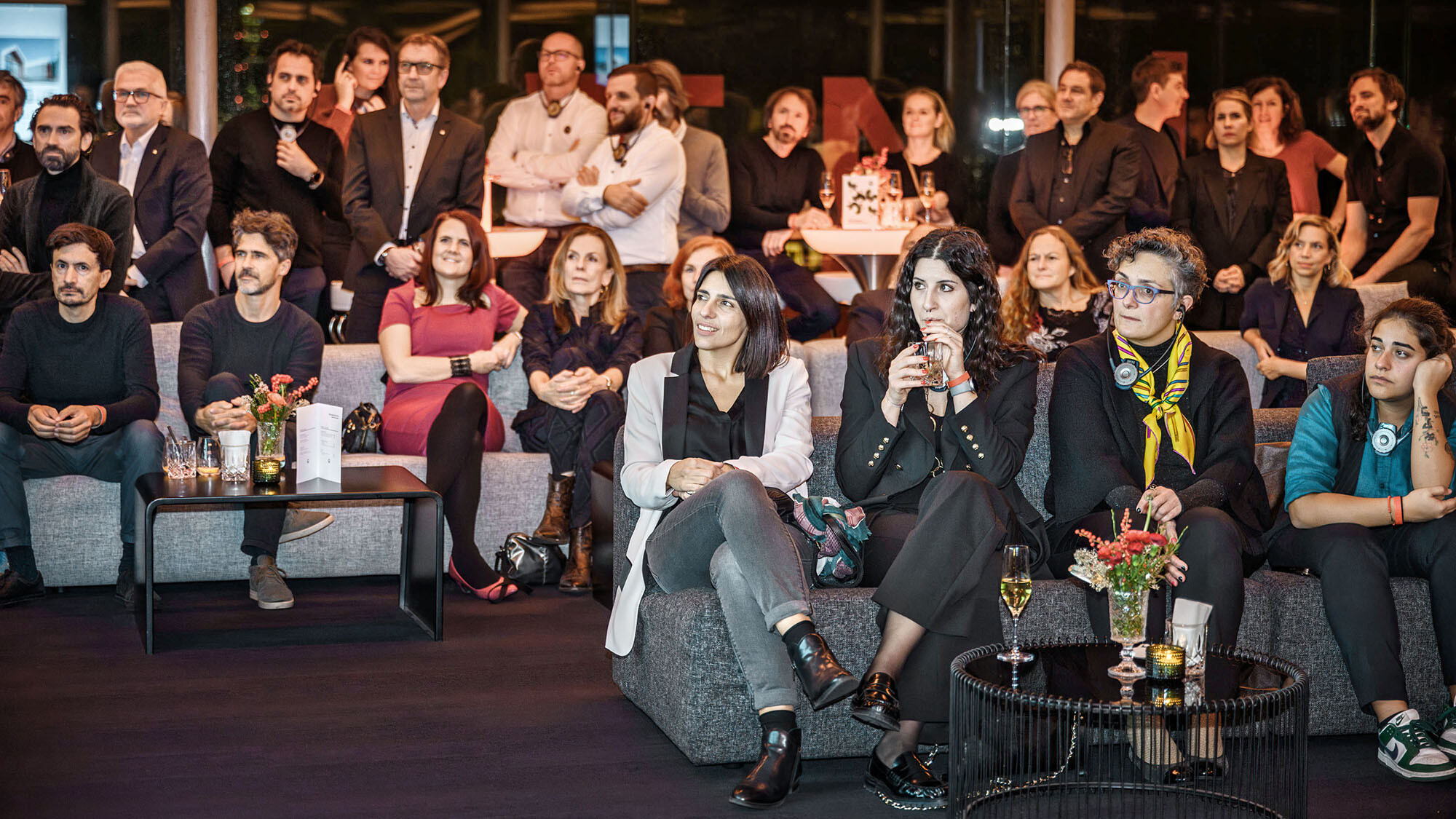 Une photo des invités de l'événement PREFARENZEN 2024, en partie debout, en partie assis sur des canapés.