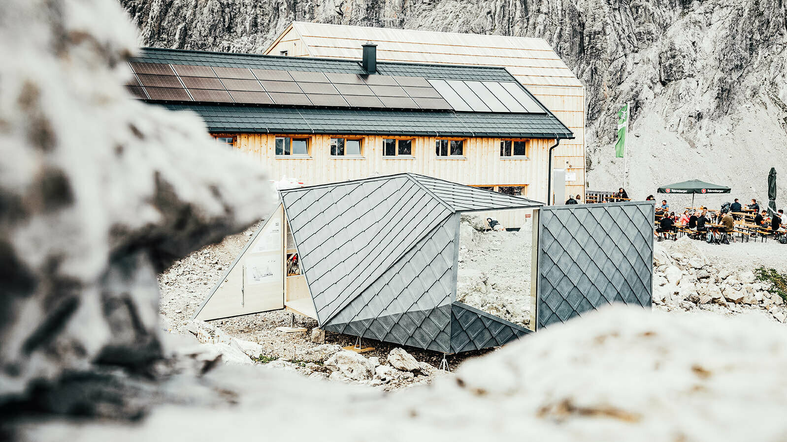 Ansicht des Wisswaks von der Rückseite. Im Hintergrund ist der Gastgarten der anliegenden Berghütte und die Berghütte selbst zu erkennen.