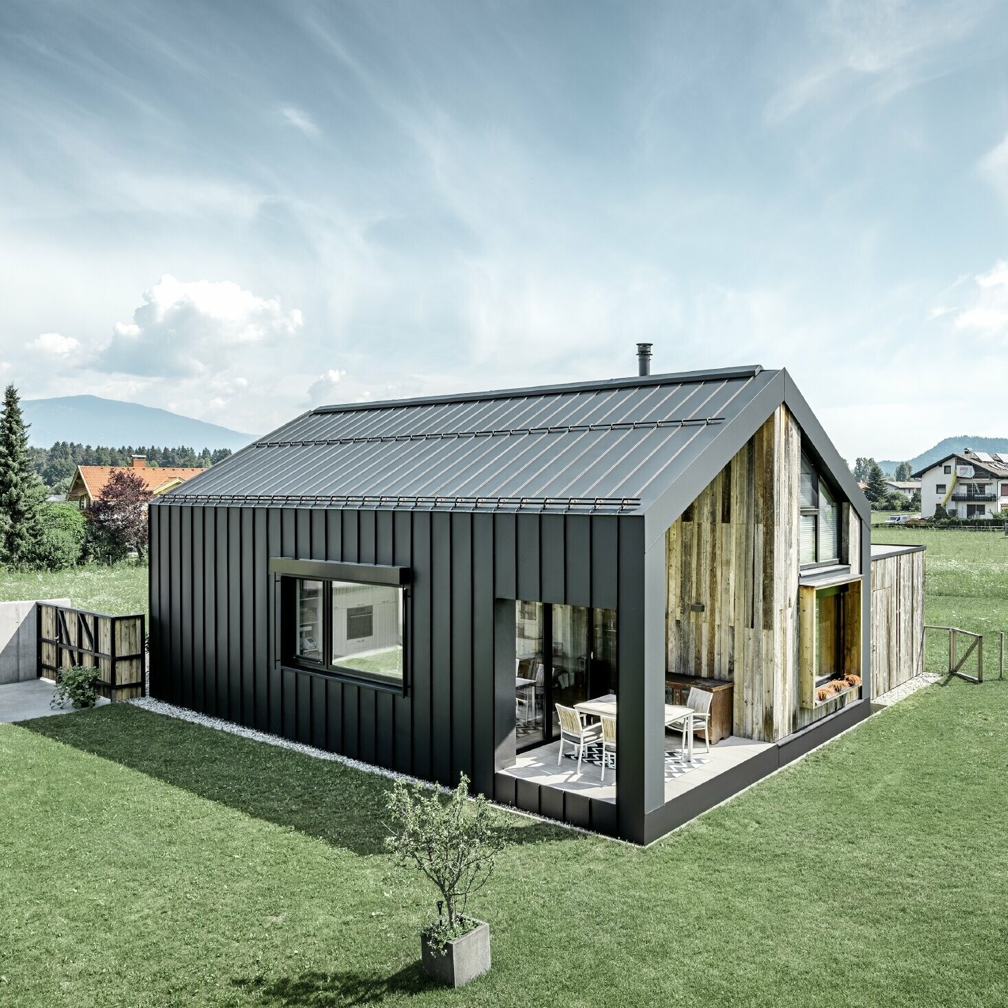 Maison individuelle avec toit à pignon ; la toiture et la façade sont recouvertes avec PREFALZ de PREFA en P.10 anthracite. Les bacs de la surface de toit se prolongent jusque sur la façade. Une partie de la façade est revêtue de bois patiné.