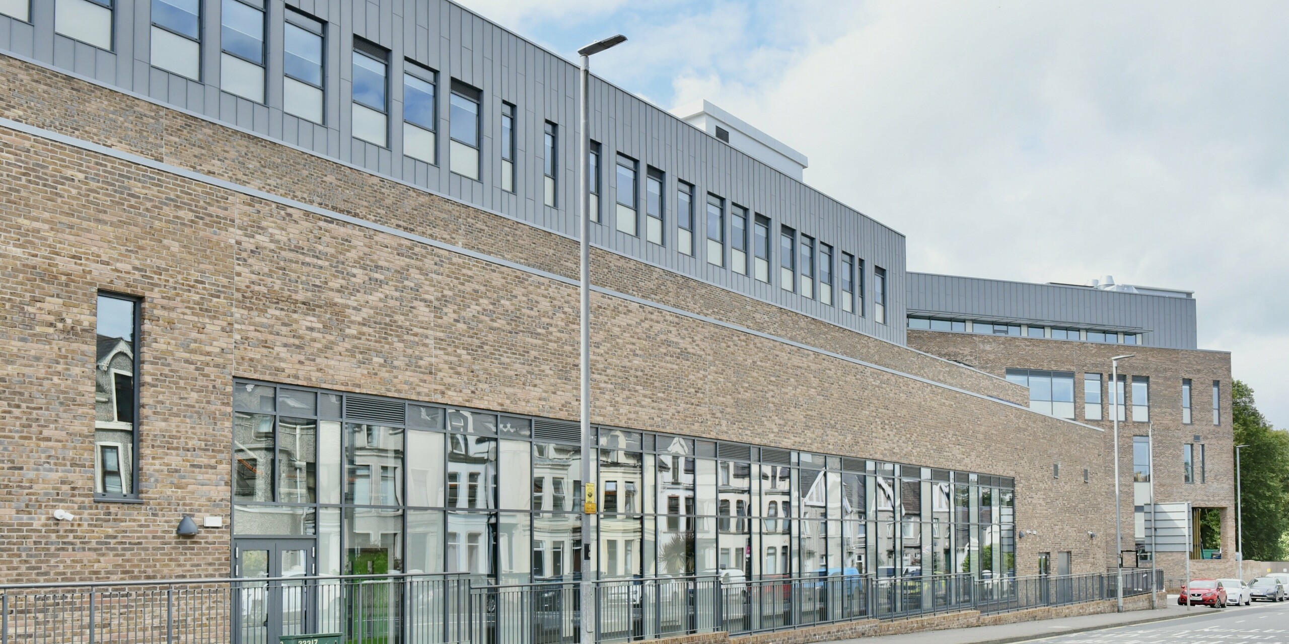 Vue de la rue du North Regional College à Coleraine, en Irlande du Nord. La façade en aluminium PREFALZ, fabriquée avec précision en gris quartz, complète l'architecture traditionnelle et s'harmonise avec l'aspect brique classique. Fonctionnalité et design se combinent pour créer un bâtiment impressionnant.