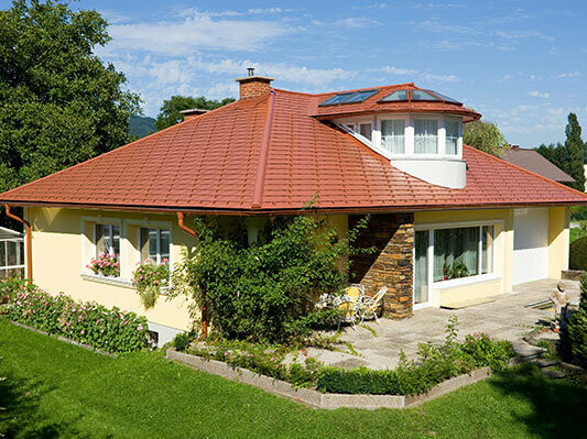 Maison individuelle avec toit à croupes et lucarne recouverte avec le bardeau PREFA en aluminium imitation tuile, rouge tuile.