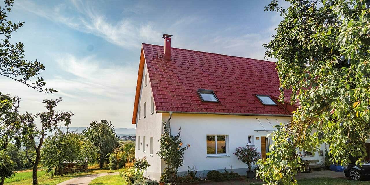 Maisonnette romantique à la campagne avec de nombreux arbres et arbustes. Recouverte avec une toiture PREFA couleur rouge oxyde.