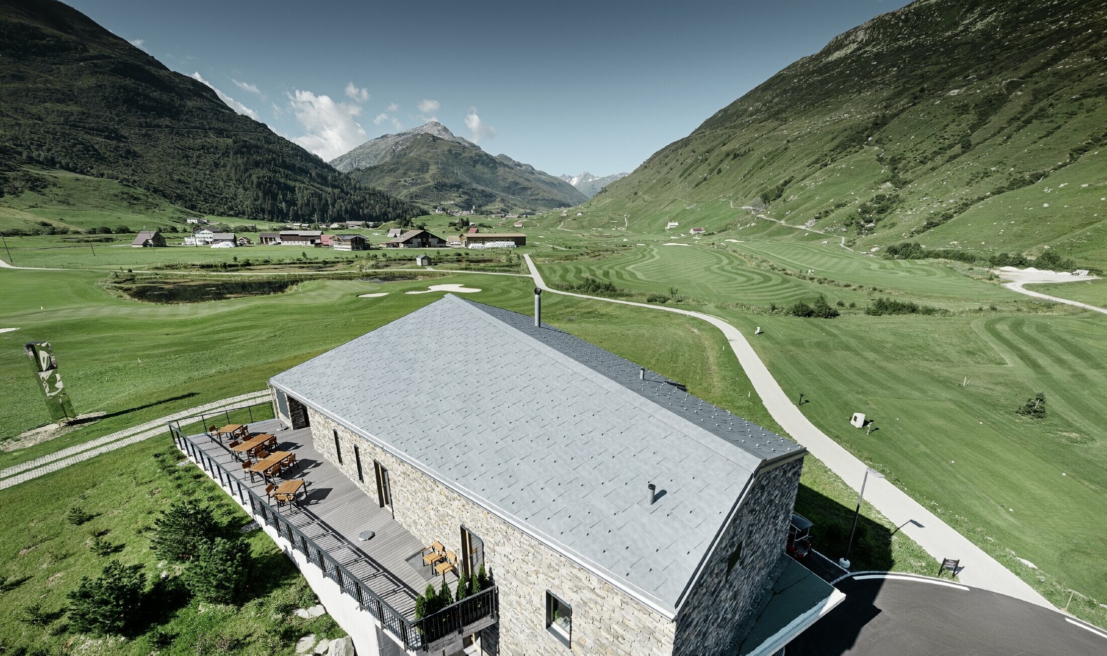 Club-house moderne du parcours de golf d’Andermatt en Suisse — Façade en pierre et panneaux de toiture FX.12 PREFA en aluminium de couleur gris pierre