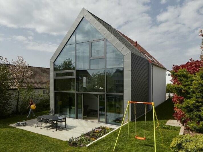 Vue de face de la Maison J à Stuttgart (Allemagne). On aperçoit un ciel nuageux en arrière-plan. La Maison J a été recouverte de Losanges de toiture 29x29 dans la teinte P.10 gris souris.