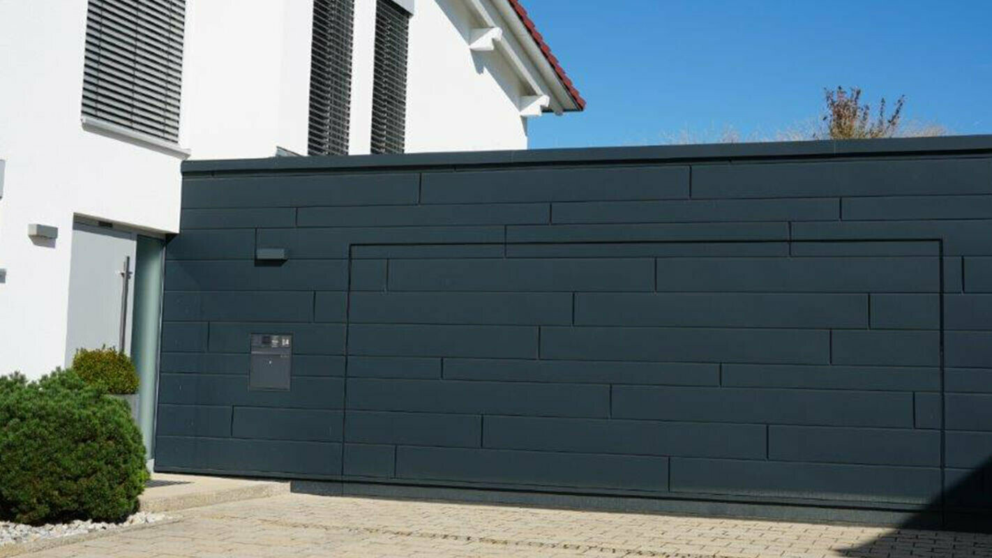 Façade d’un garage après la rénovation à l’aide de Sidings PREFA couleur anthracite. La porte de garage est alignée avec la façade 