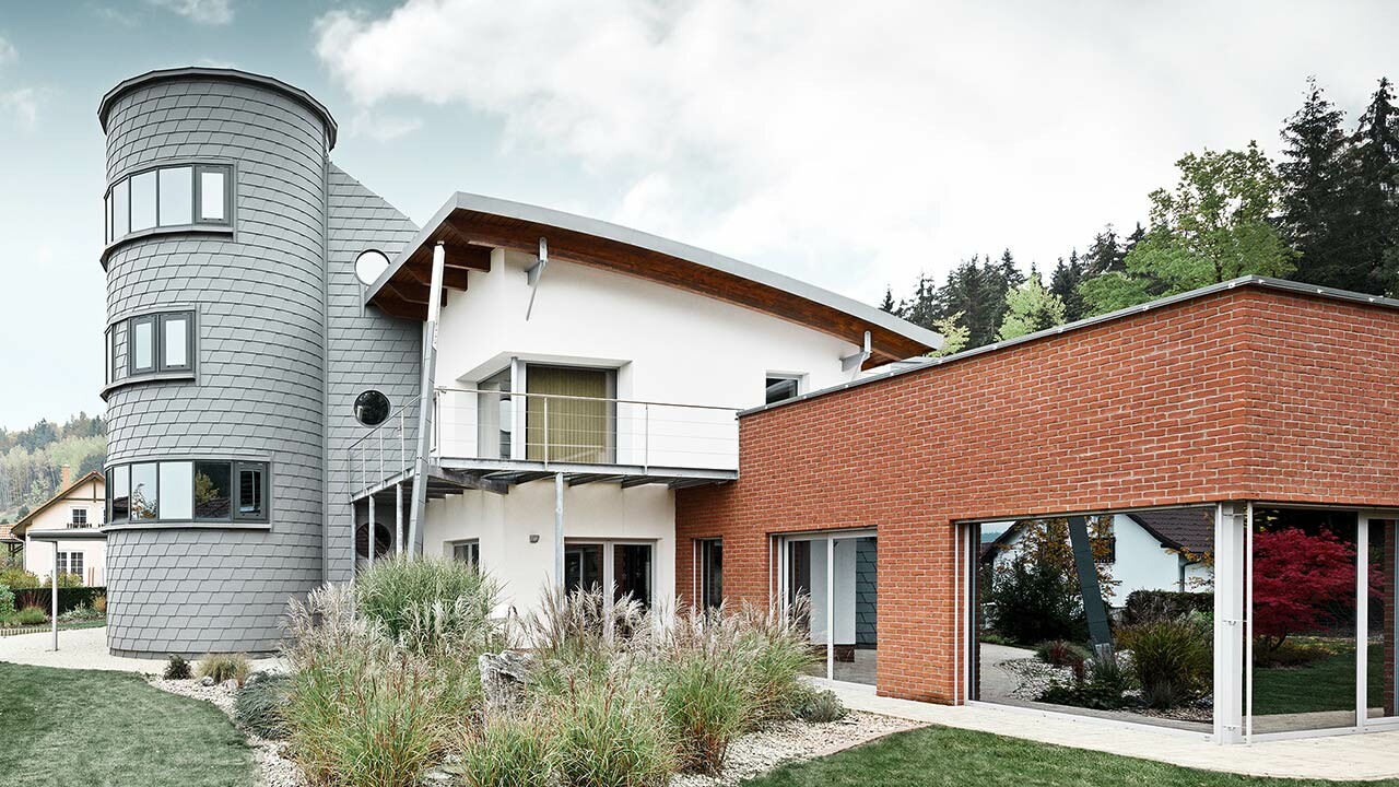 Maison individuelle avec extension de tour ; la tour ronde est revêtue du bardeau de façade PREFA couleur gris quartz 