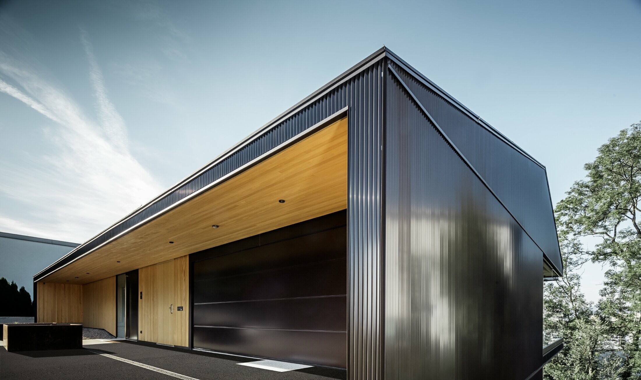 Entrée de garage d’une maison individuelle, la façade est recouverte de profils triangle PREFA couleur brun foncé. 