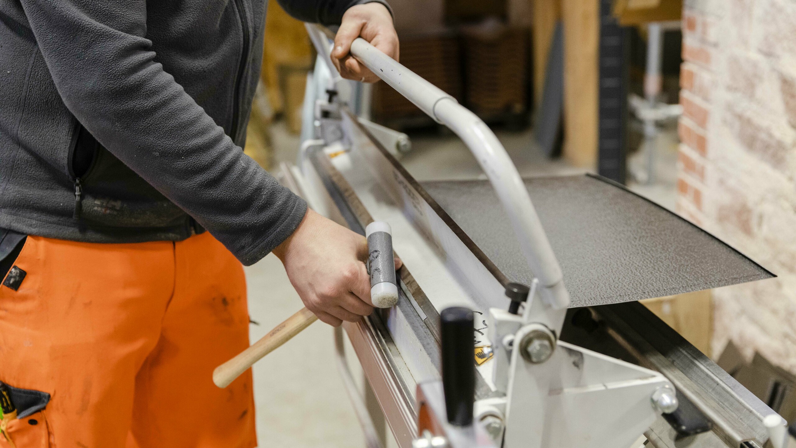 Un participant manipule une machine spécialisée, posant ou coupant une tôle métallique dans un atelier.