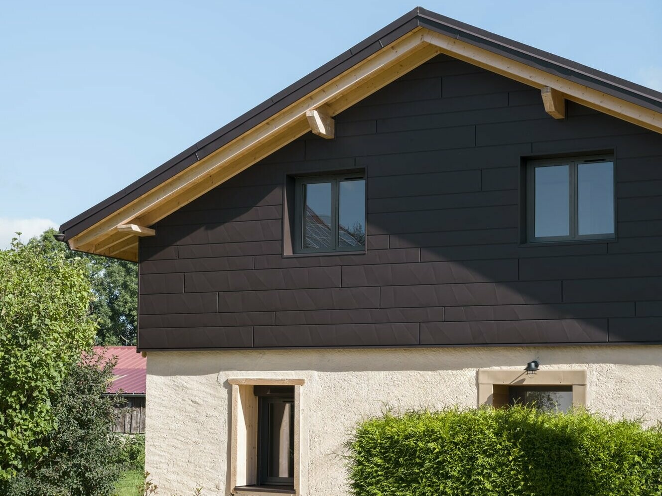 Vue de face de cette maison familiale rénovée, on aperçoit la façade avec en partie haute le Siding PREFA allié à la pierre naturelle en partie basse