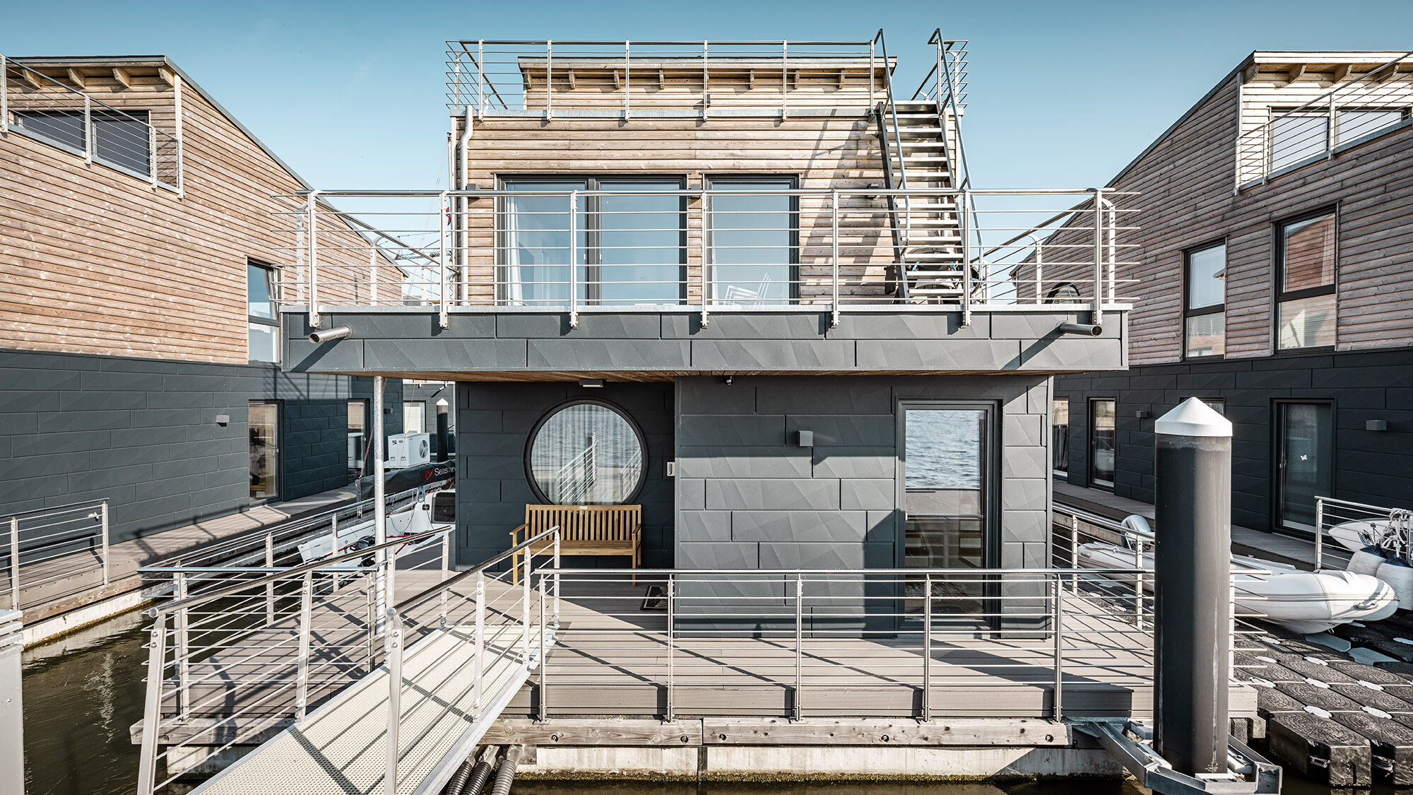 Une des maisons en vue rapprochée depuis une perspective normale : les façades en bois et en aluminium sont visibles tandis que la Schlei se reflète dans les fenêtres.