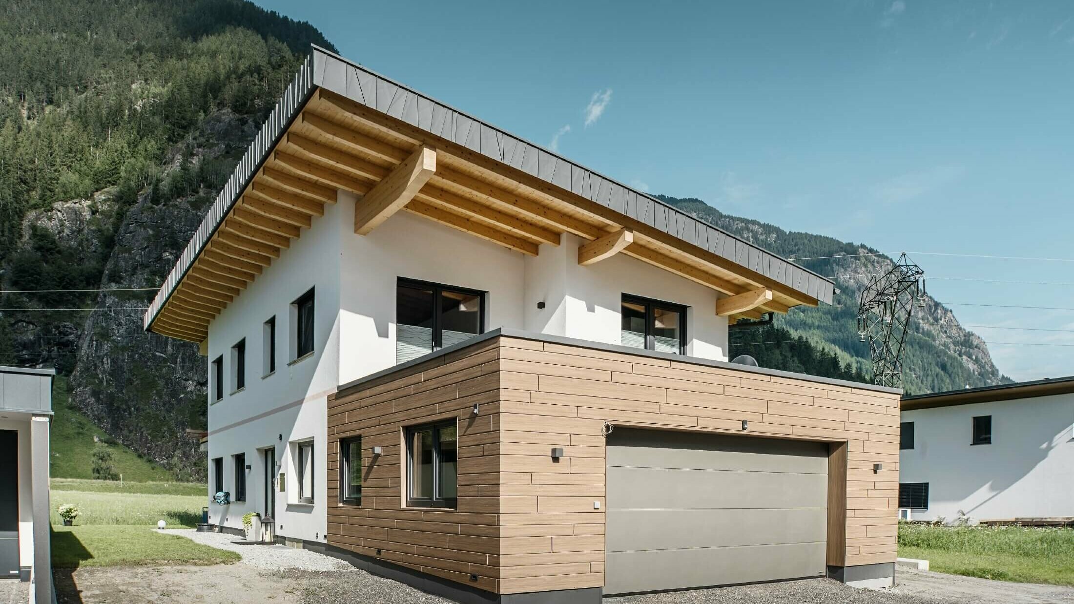 Garage d’une habitation avec Sidings PREFA d’aspect bois dans la teinte « noyer foncé ». Des montagnes se trouvent en arrière-plan. 