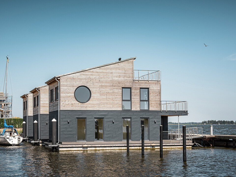Vue latérale de trois des « maisons flottantes » revêtues de bois et d’aluminium dans le port du Pionierhafen de Schleswig.
