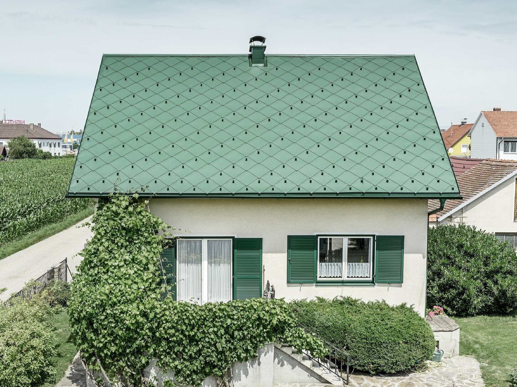 Toit à pignon de maison individuelle classique avec couverture en aluminium vert mousse et volets verts Le toit est recouvert de losanges de toiture PREFA 44 × 44 en P.10 vert mousse.