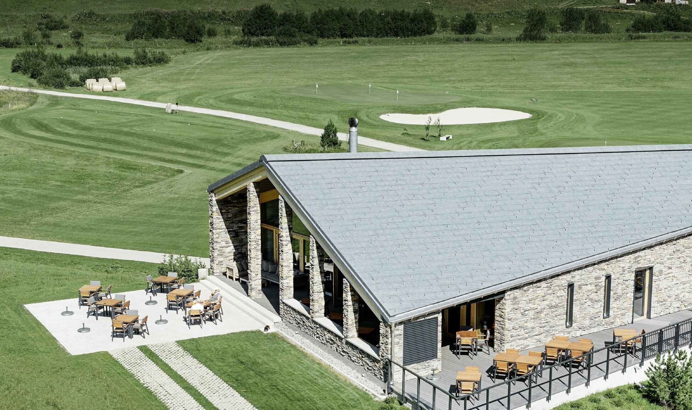 Club-house moderne du parcours de golf d’Andermatt en Suisse — Façade en pierre et panneaux de toiture FX.12 PREFA en aluminium de couleur gris pierre