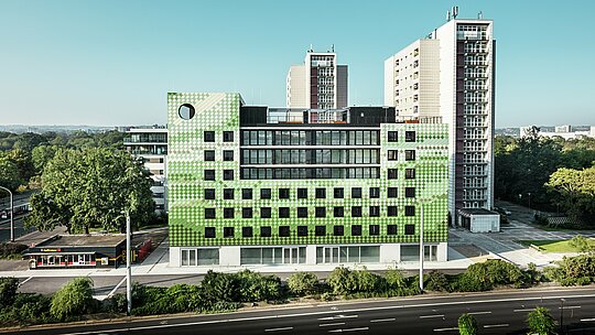 Vue latérale de l'immeuble résidentiel et commercial "Pick-Nick" sur la Straßburger Platz à Dresde avec une façade PREFA frappante en aluminium robuste. Un bâtiment moderne aux lignes épurées et aux grandes fenêtres s'intègre dans l'environnement urbain entre gratte-ciels résidentiels et espaces verts. Le design distinctif met des accents architecturaux.