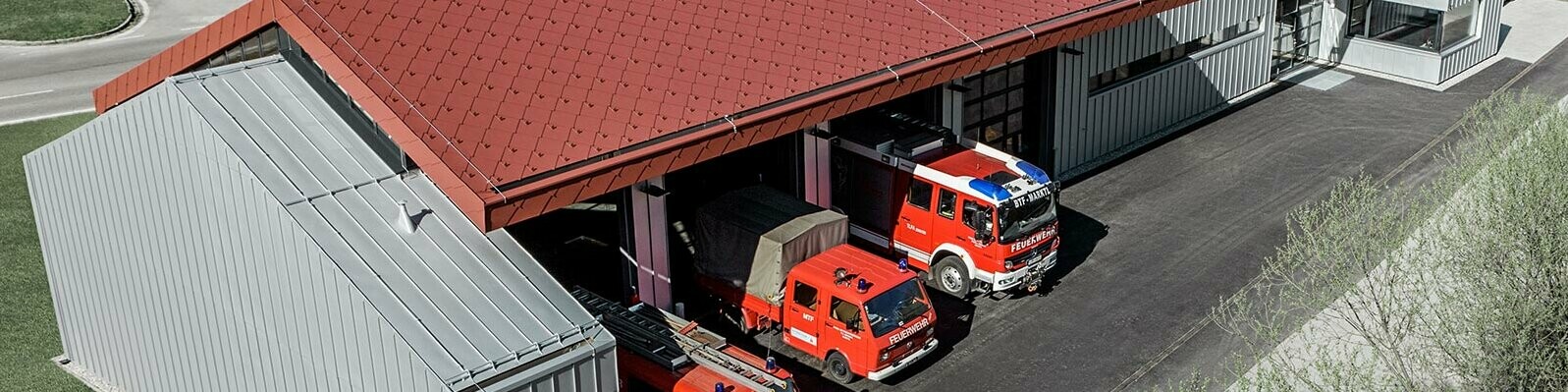 Véhicules de pompiers dans la caserne de la société PREFA. Le bâtiment est doté d’une toiture en losanges rouges (aluminium non inflammable) et d’une façade en aluminium.