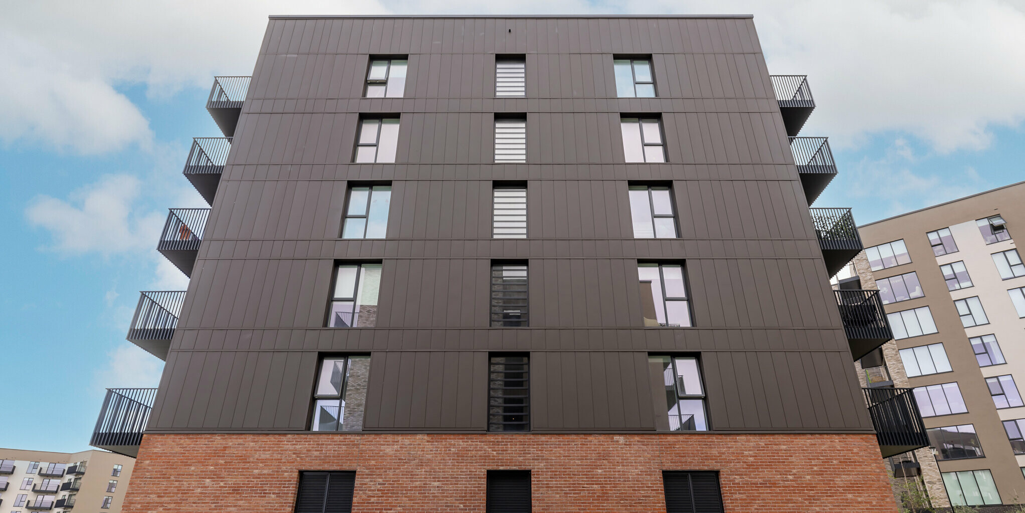 Vue plongeante sur les appartements Citywest à Dublin. Les 700 m² de bardages PREFA posés verticalement en P.10 brun se combinent avec la façade en briques pour former un ensemble harmonieux et durable. Les panneaux modernes en aluminium de PREFA garantissent durabilité et design.