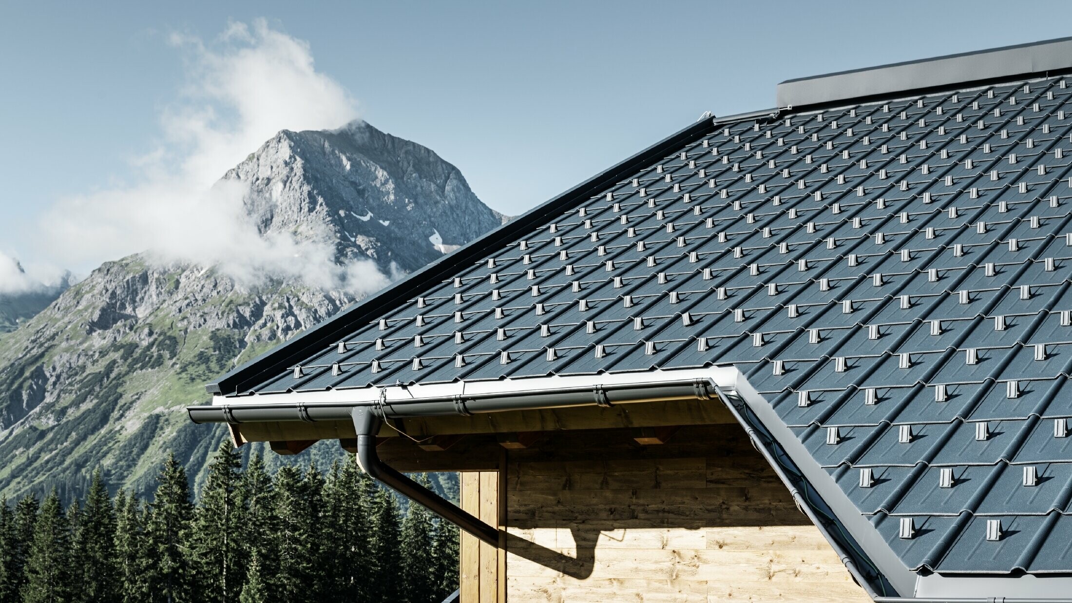 Maison en bois à la montagne, la toiture est recouverte avec la tuile PREFA couleur anthracite avec gouttière PREFA et façade en bois