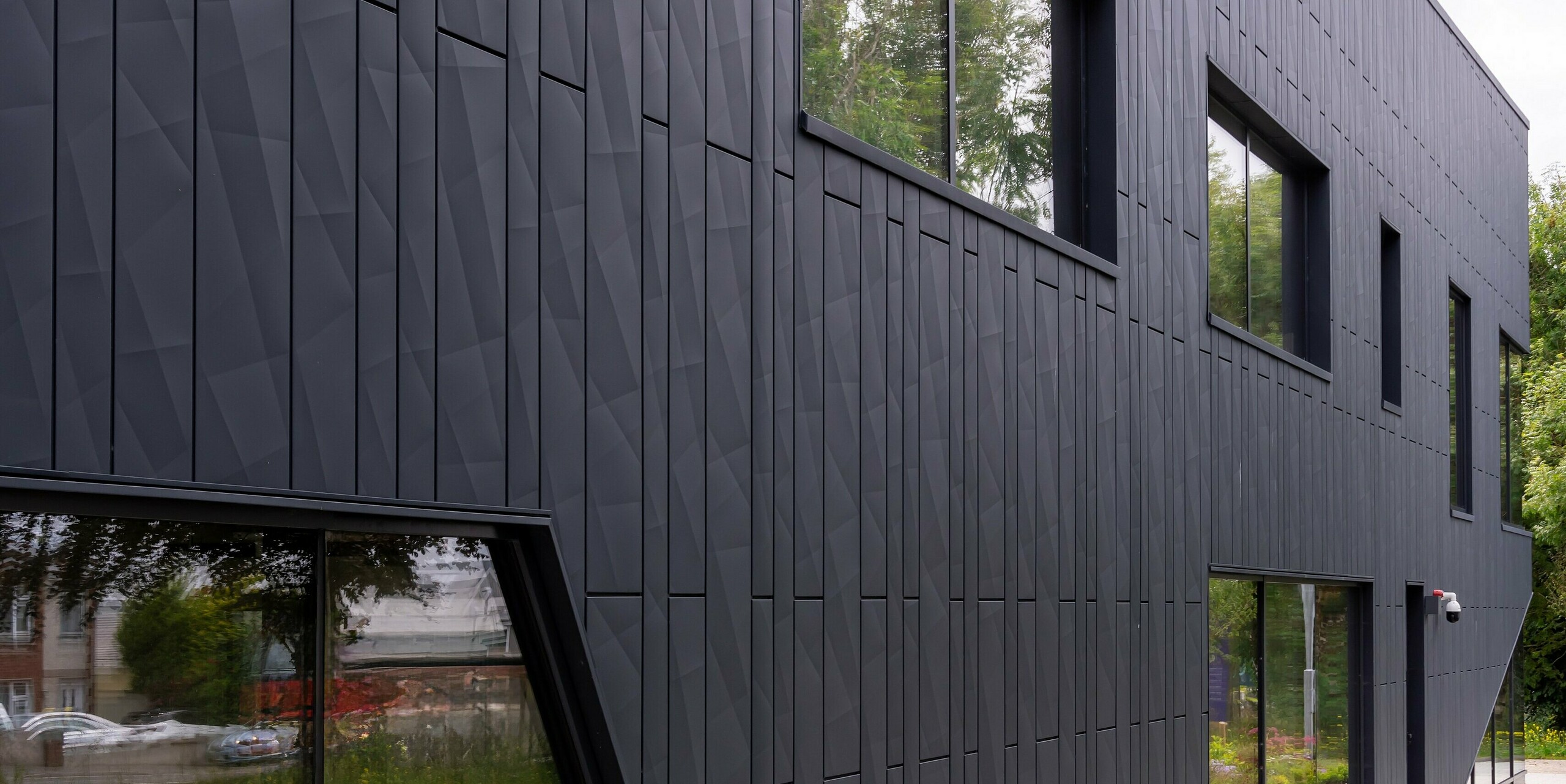 Vue arrière du bâtiment CREW à Galway, Irlande, avec une vue détaillée des panneaux de façade PREFA Siding.X en anthracite P.10. Le revêtement en aluminium à structure géométrique confère à la façade un aspect moderne et dynamique. Les surfaces vitrées individuelles et les lignes claires du bâtiment complètent le design minimaliste, tandis que les espaces verts environnants complètent l'ensemble.