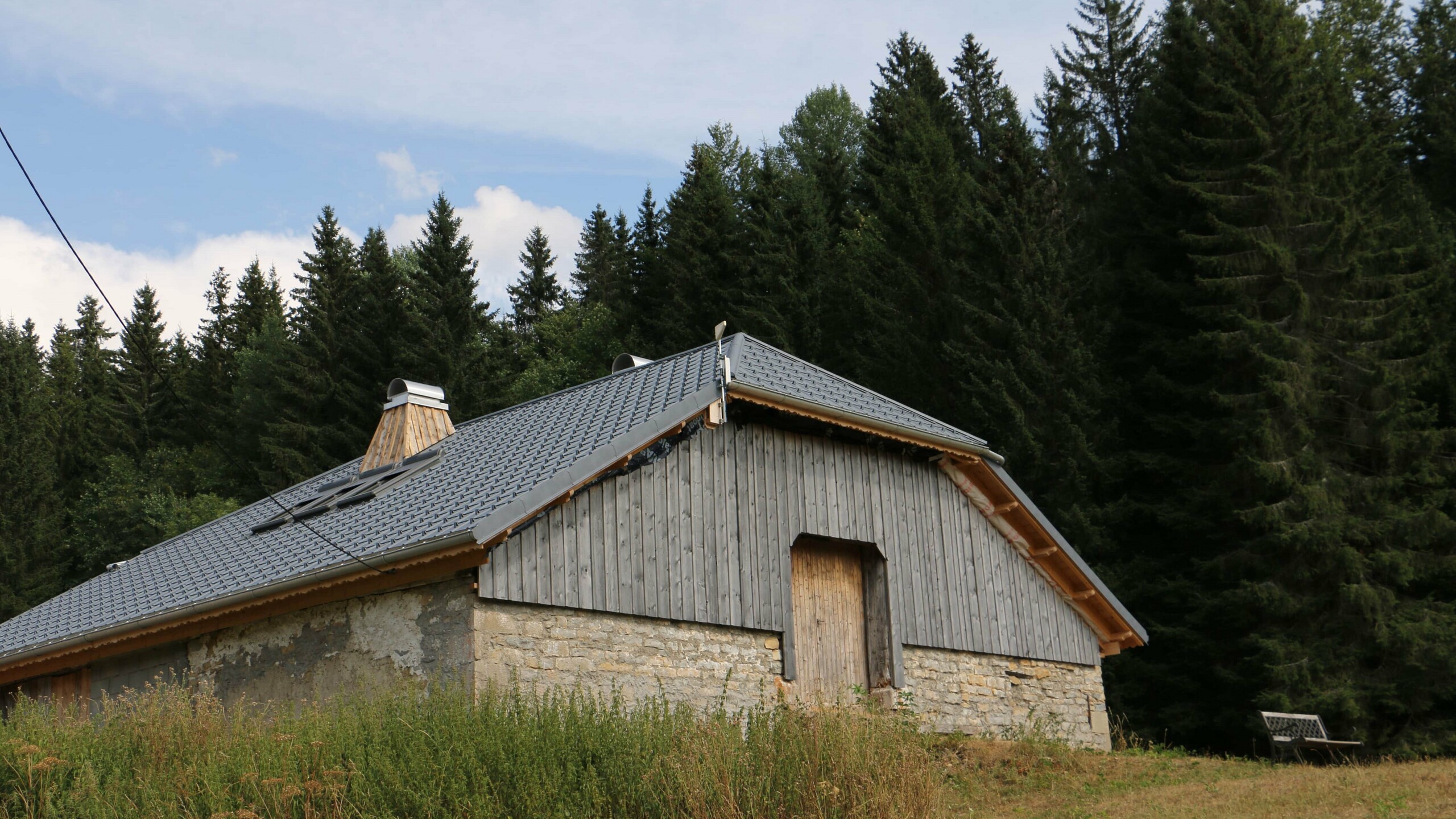 Vue lointaine du chalet rénové en pleine nature avec la tuile en aluminium prefa dans la teinte P.10 gris pierre