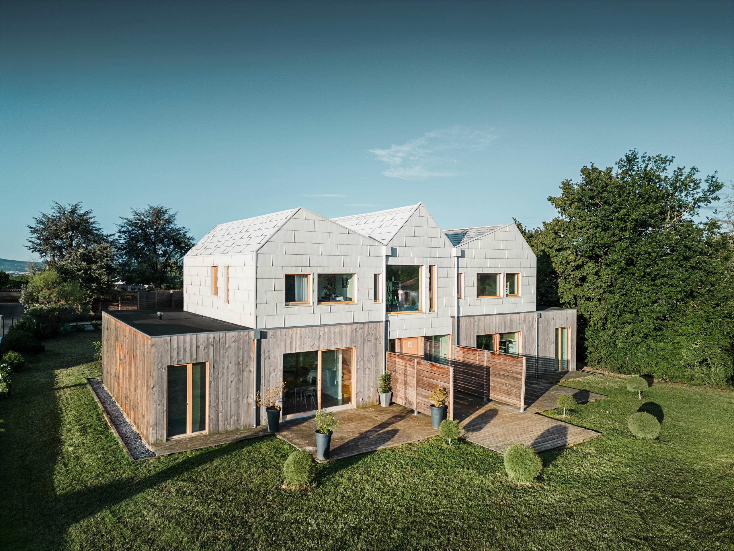 Maison jumelée avec une façade composée de panneaux en aluminium FX.12 de PREFA, combinés avec des éléments en bois naturel dans la zone inférieure. Le design crée une harmonie parfaite entre l’architecture moderne et la nature.