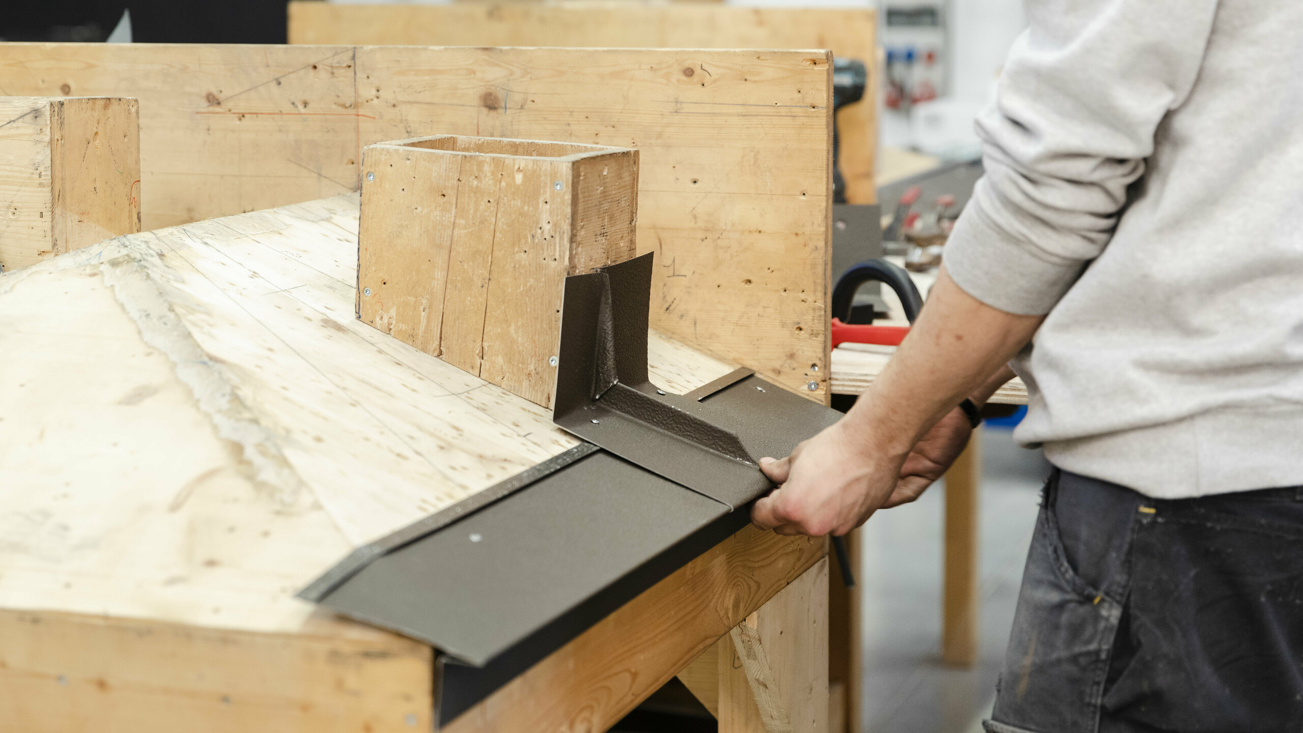 Un homme manipule une tôle métallique près d'un cadre en bois, se préparant à la fixer ou à la plier.