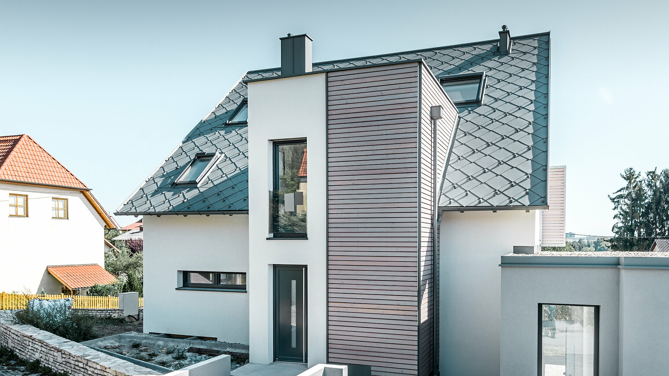 La maison individuelle avec toit à deux pans à Leonding a été entièrement rénovée. La surface de toit a été recouverte de losanges de toiture 44 × 44 PREFA couleur gris souris avec arrêts neige. Le choix s’est porté sur la gouttière suspendue de PREFA, également couleur gris souris. 