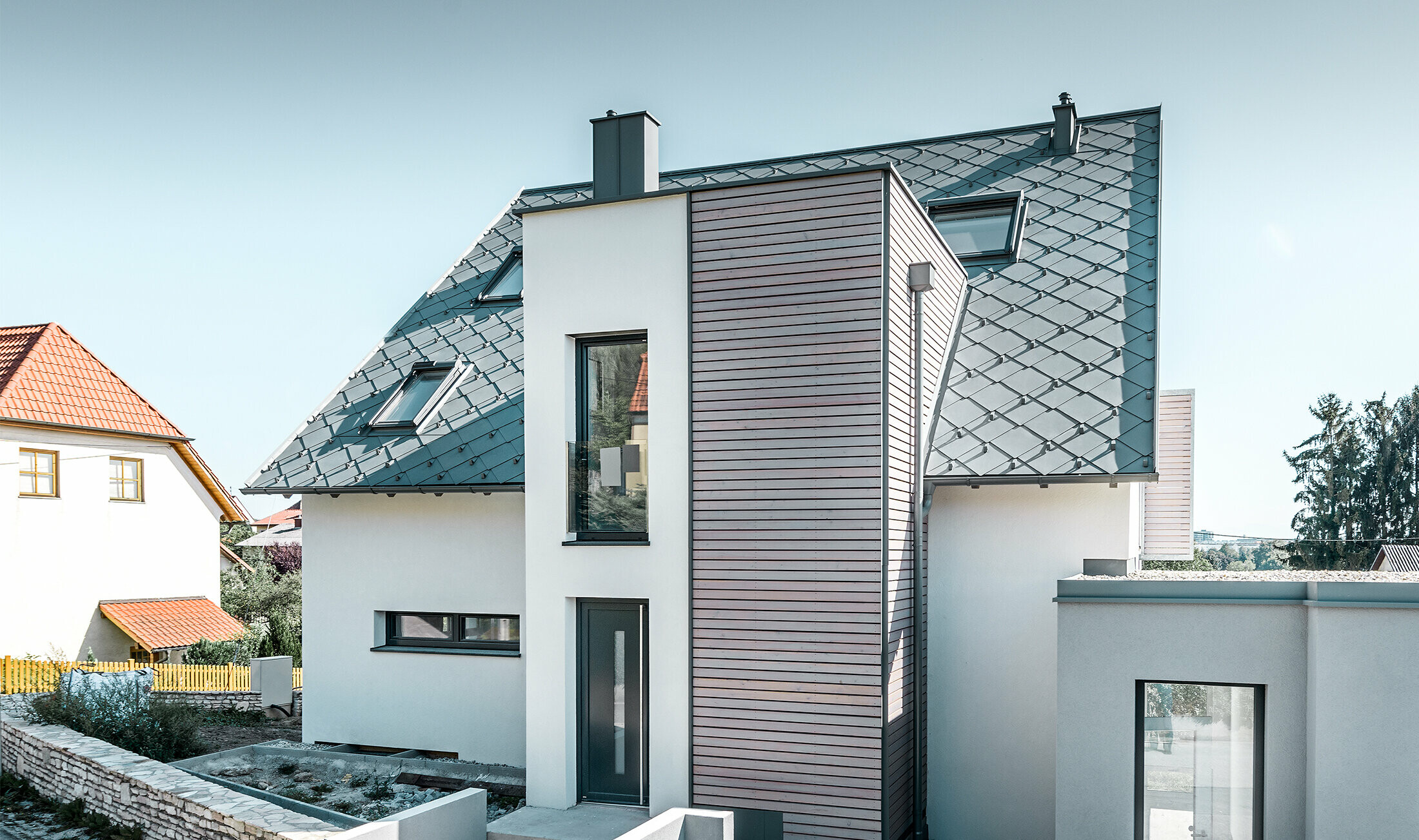 La maison individuelle avec toit à deux pans à Leonding a été entièrement rénovée. La surface de toit a été recouverte de losanges de toiture 44 × 44 PREFA couleur gris souris avec arrêts neige. Le choix s’est porté sur la gouttière suspendue de PREFA, également couleur gris souris. 