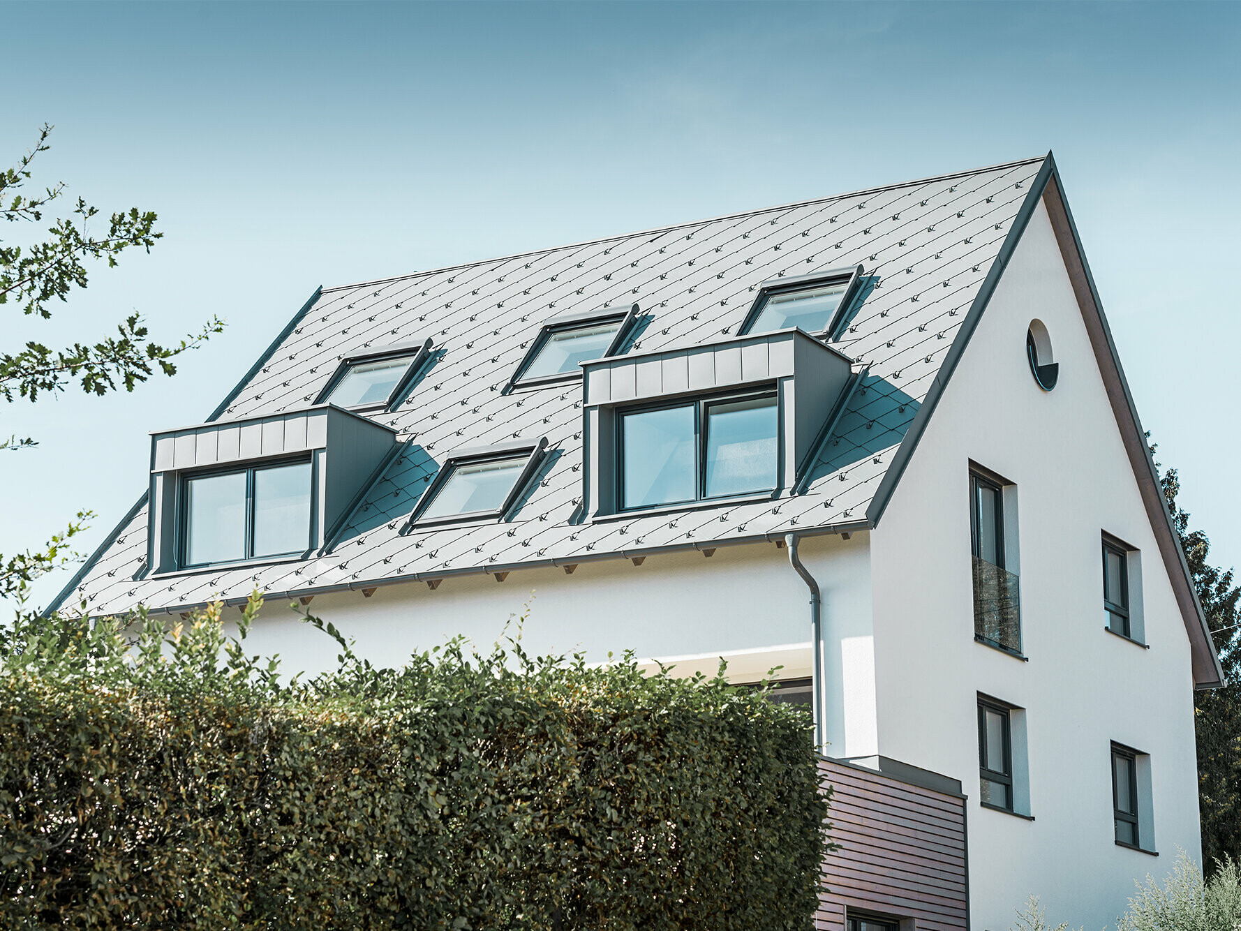 Rénovation d’un toit à deux pans avec deux lucarnes et quatre fenêtres de toit ; la toiture a été recouverte de losanges de toiture 44 × 44 PREFA couleur gris souris. Le choix s’est porté sur une gouttière suspendue PREFA également couleur gris souris. 