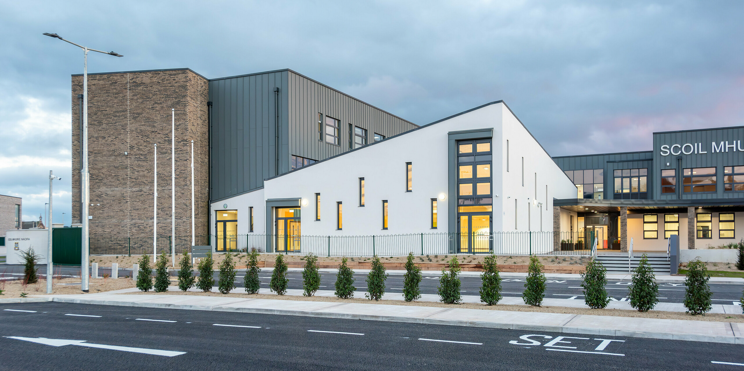 L'école moderne Scoil Mhuire Naofa à Carrigtwohill, en Irlande, avec son élégante façade en aluminium PREFALZ en P.10 gris souris. Le design lumineux et minimaliste associe des lignes épurées à un toit à joint debout de haute qualité, tandis que le paysage environnant et la nouvelle route d'accès soulignent le caractère moderne de l'établissement d'enseignement. Les intérieurs éclairés attirent le regard sur les fenêtres spacieuses.