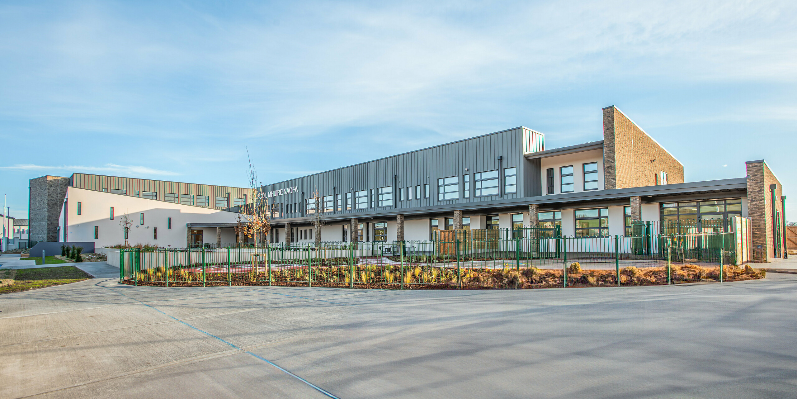 Perspective grand angle de Scoil Mhuire Naofa à Carrigtwohill, Irlande. Le bâtiment scolaire allie une architecture moderne à une façade en aluminium PREFALZ en P.10 gris souris. Le toit à joint debout, durable et résistant aux intempéries, souligne l'élégance fonctionnelle, tandis que les espaces extérieurs bien entretenus soulignent le caractère moderne de l'école.