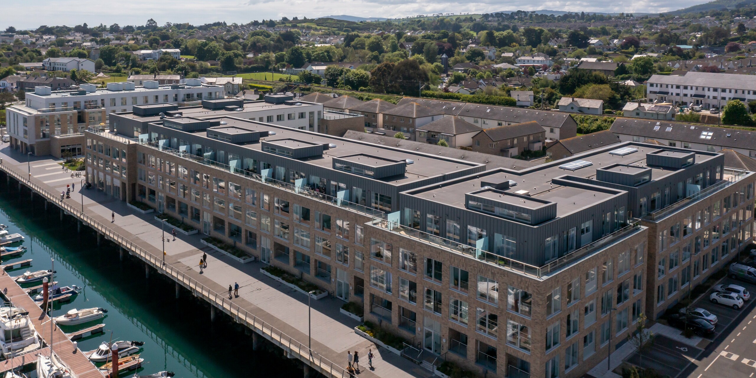 Vue panoramique grand angle de Marina Village Greystones à Wicklow, Irlande - Développement résidentiel moderne en bord de mer avec un emplacement direct sur la marina. Le complexe immobilier est revêtu de PREFALZ robuste dans les couleurs P.10 Prefa blanc et P.10 gris souris. L'architecture élégante comprend de grandes façades vitrées, des balcons spacieux et une façade en tôle de haute qualité. L'utilisation de l'aluminium PREFALZ offre une protection durable et un aspect attrayant. Entouré de paysages pittoresques, le projet résidentiel est synonyme de vie exclusive au bord de la mer.