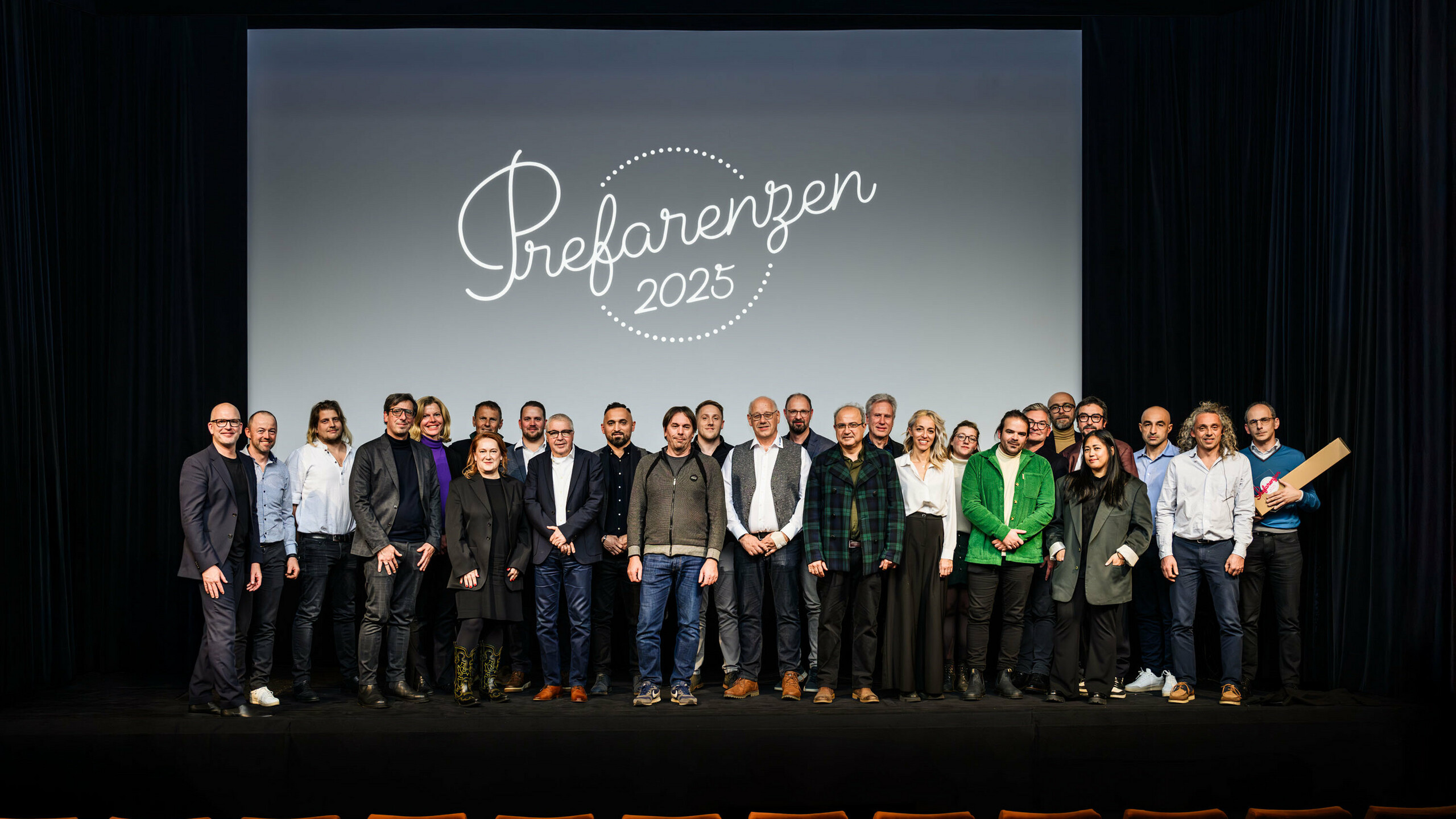 Photo de groupe lors de la première édition de la Cérémonie des PREFARENZEN 2025 au cinéma municipal de Vienne : Jürgen Jungmair, directeur marketing de PREFA, entouré d’intervenants et d’invités se tenant devant le logo de l’événement « PREFARENZEN 2025 » projeté sur l’écran. Les participants venus des quatre coins de l’Europe représentent les secteurs de l’architecture, de l’urbanisme, de la construction et des médias.