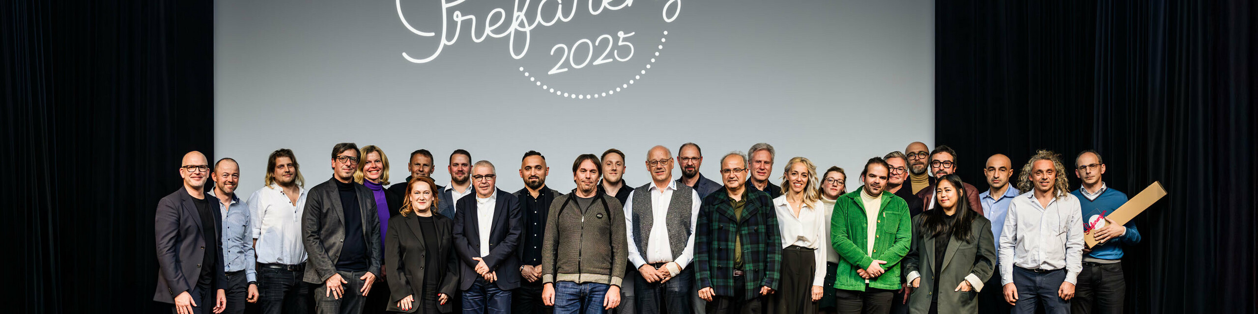 Photo de groupe lors de la première édition de la Cérémonie des PREFARENZEN 2025 au cinéma municipal de Vienne : Jürgen Jungmair, directeur marketing de PREFA, entouré d’intervenants et d’invités se tenant devant le logo de l’événement « PREFARENZEN 2025 » projeté sur l’écran. Les participants venus des quatre coins de l’Europe représentent les secteurs de l’architecture, de l’urbanisme, de la construction et des médias.