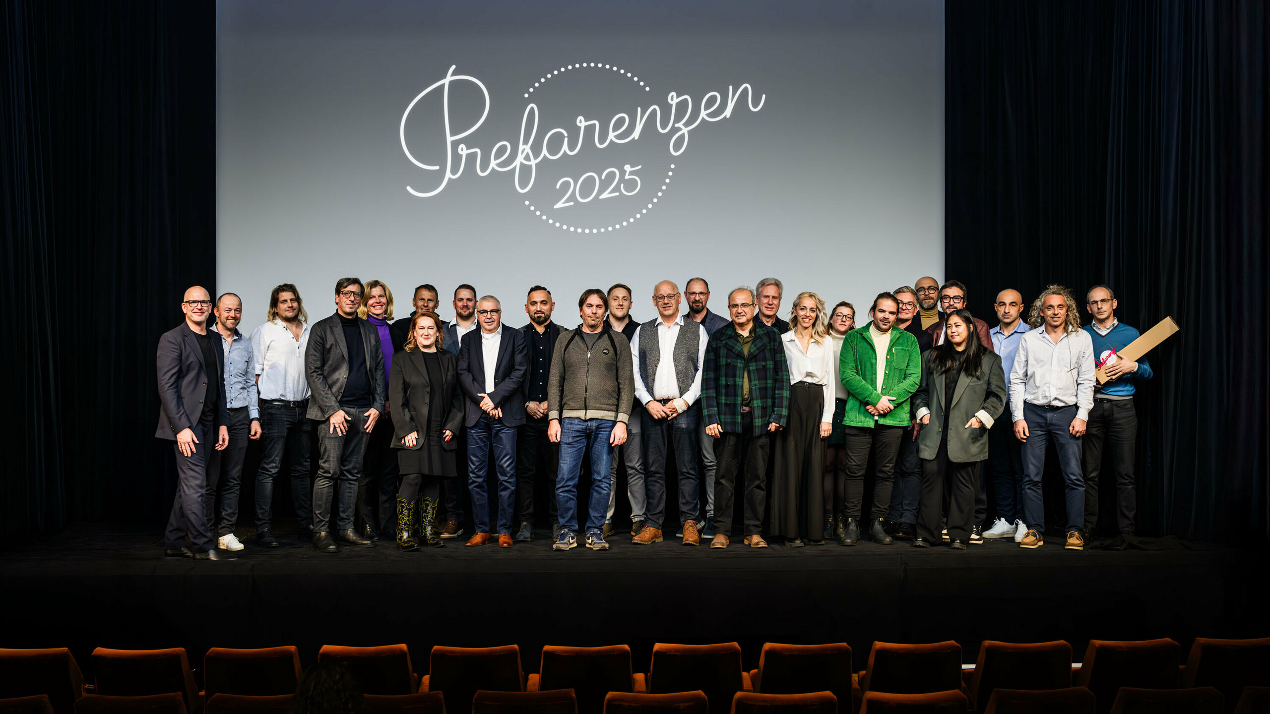 Photo de groupe lors de la première édition de la Cérémonie des PREFARENZEN 2025 au cinéma municipal de Vienne : Jürgen Jungmair, directeur marketing de PREFA, entouré d’intervenants et d’invités se tenant devant le logo de l’événement « PREFARENZEN 2025 » projeté sur l’écran. Les participants venus des quatre coins de l’Europe représentent les secteurs de l’architecture, de l’urbanisme, de la construction et des médias.