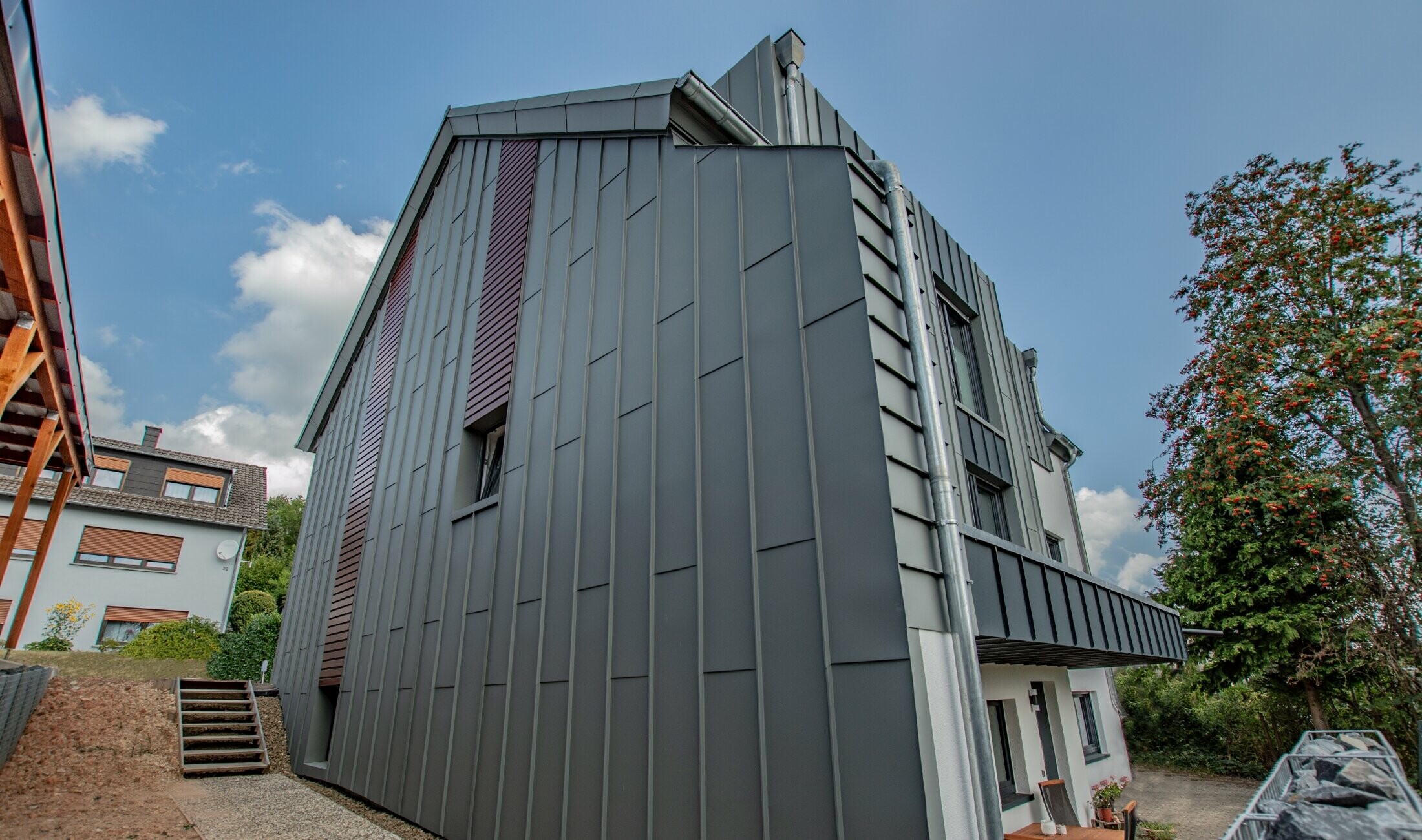 Conception de façade avec façade à agrafage angulaire vertical en gris souris et panneaux de façade posés à l’horizontale, couleur bois foncé. Toute la façade a été réalisée en aluminium par PREFA.