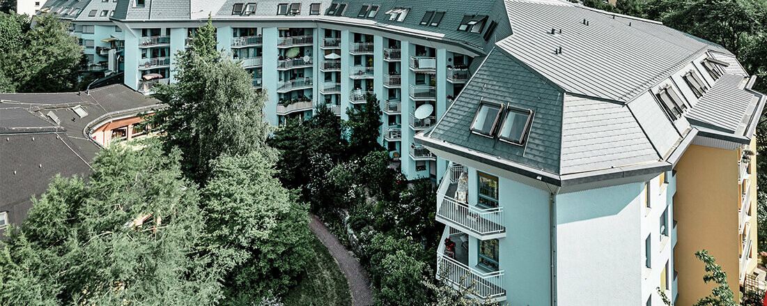 Grand bâtiment d’habitation consacré à l’accueil des personnes âgés, recouvert de bardeaux de toiture et Prefalz PREFA couleur gris pierre, avec de nombreux balcons.